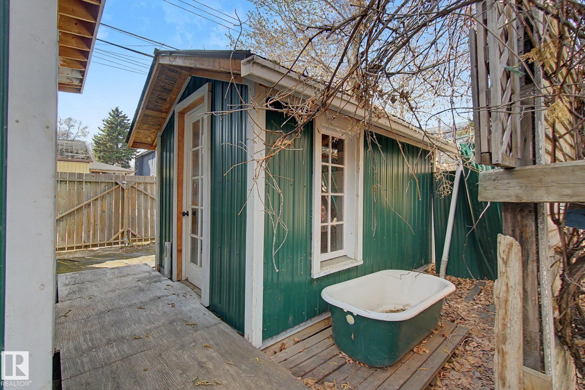 Detached shed featuring green corrugated siding, white trim, and a white-framed glass-paneled door - 11512 122 St, Edmonton, AB - Outdoor With Exterior
