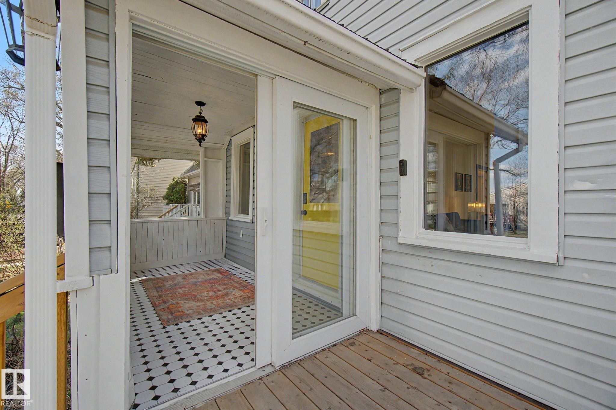 Inviting screened porch featuring black and white patterned tile flooring, a hanging lantern light fixture, and white painted railings - 11512 122 St, Edmonton, AB - Outdoor With Exterior