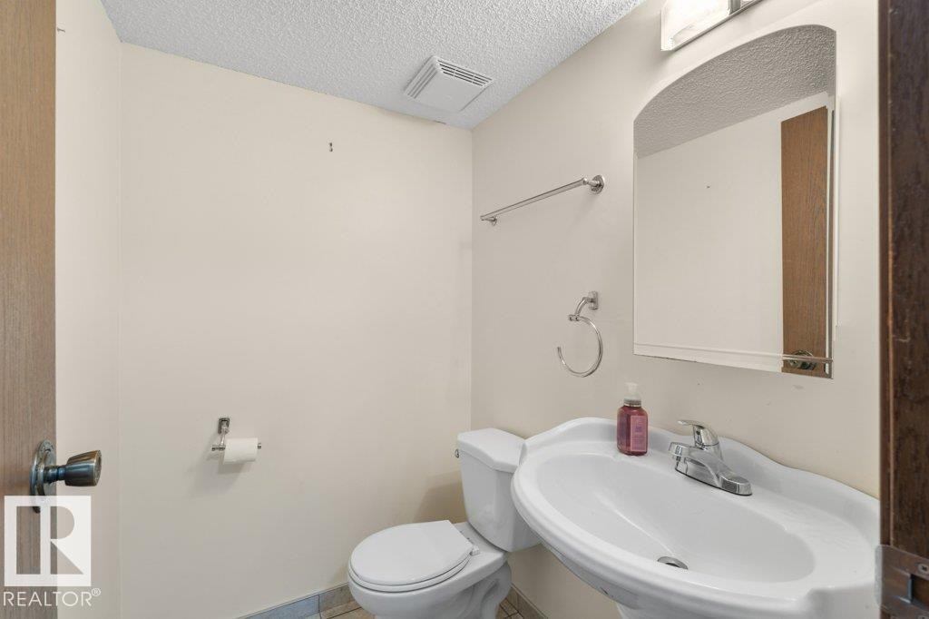 The bathroom features a white pedestal sink with a chrome faucet, a toilet, and an arched mirror - 17313 60 Avenue, Edmonton, AB - Indoor Photo Showing Bathroom