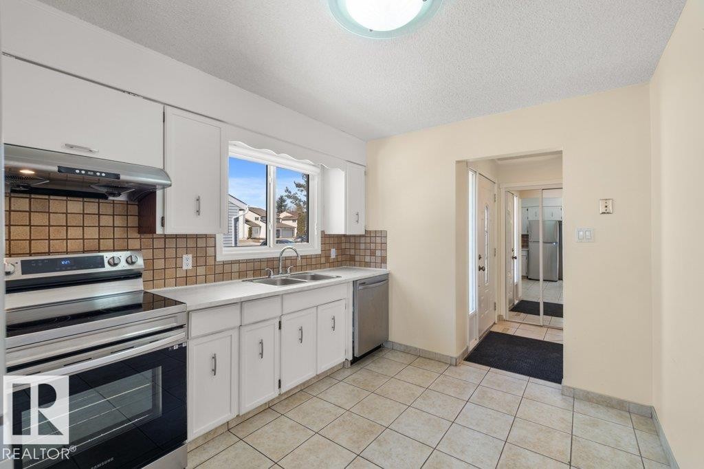 The kitchen features white cabinetry, a tiled backsplash, and stainless steel appliances including a range and dishwasher - 17313 60 Avenue, Edmonton, AB - Indoor Photo Showing Kitchen With Double Sink