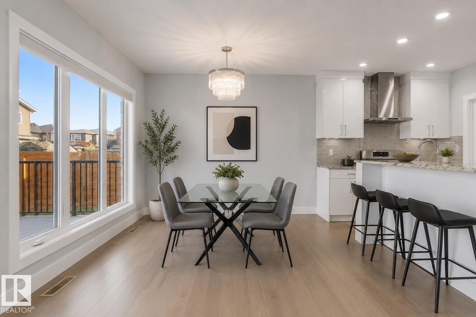 Open-concept living space featuring wood-finish flooring, a contemporary chandelier, and a large window overlooking the exterior patio. Virtually Staged. - 635 42 Street, Edmonton, AB - Indoor