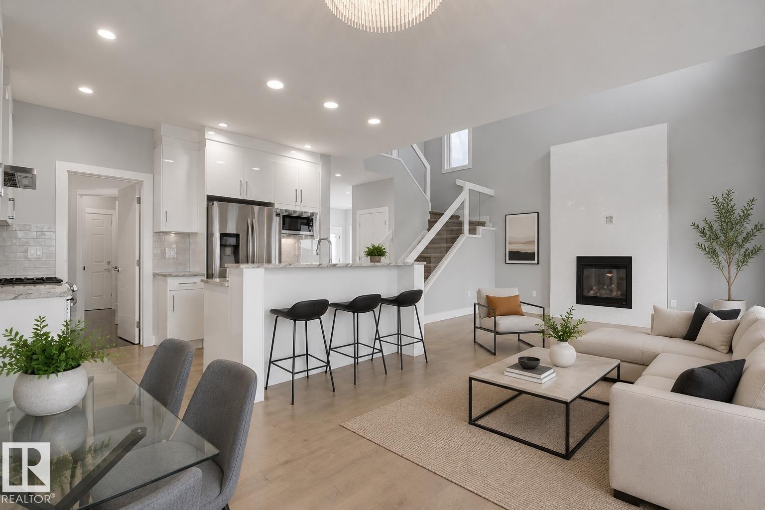 Open-concept living space featuring a gourmet kitchen, integrated breakfast bar, tall fireplace, light wood-finish flooring, and a modern staircase with glass railing. Virtually Staged. - 635 42 Street, Edmonton, AB - Indoor