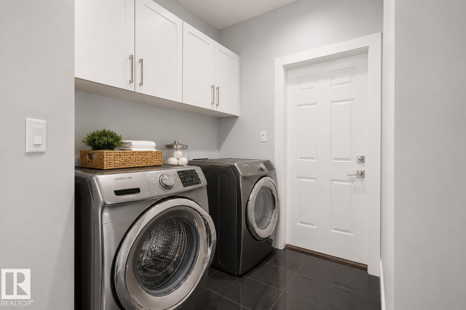 Utility area with dark tile flooring, white shaker-style cabinetry, and a paneled door with brushed nickel hardware. Virtually Staged. - 635 42 Street, Edmonton, AB - Indoor Photo Showing Laundry Room