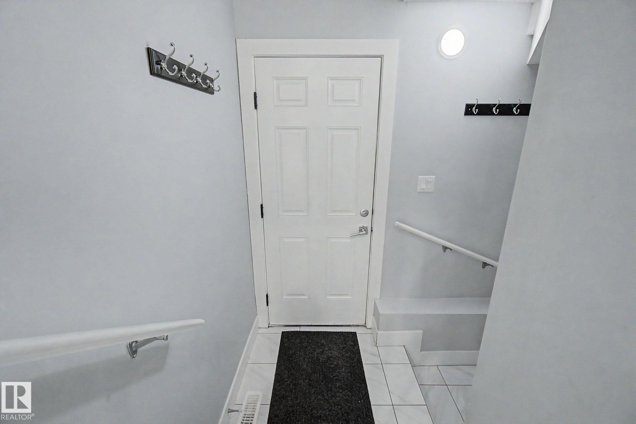 Entryway featuring a paneled door with polished hardware, white tile flooring, and white painted walls. - 635 42 Street, Edmonton, AB - Indoor Photo Showing Other Room
