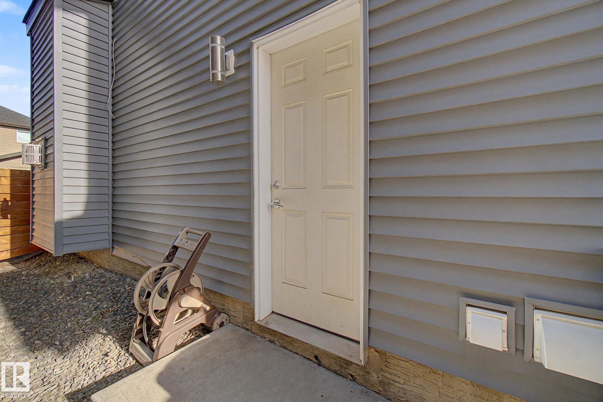 Gray horizontal siding exterior with a cream-colored entry door, concrete pad, and external wall lighting fixture - 635 42 Street, Edmonton, AB - Outdoor With Exterior