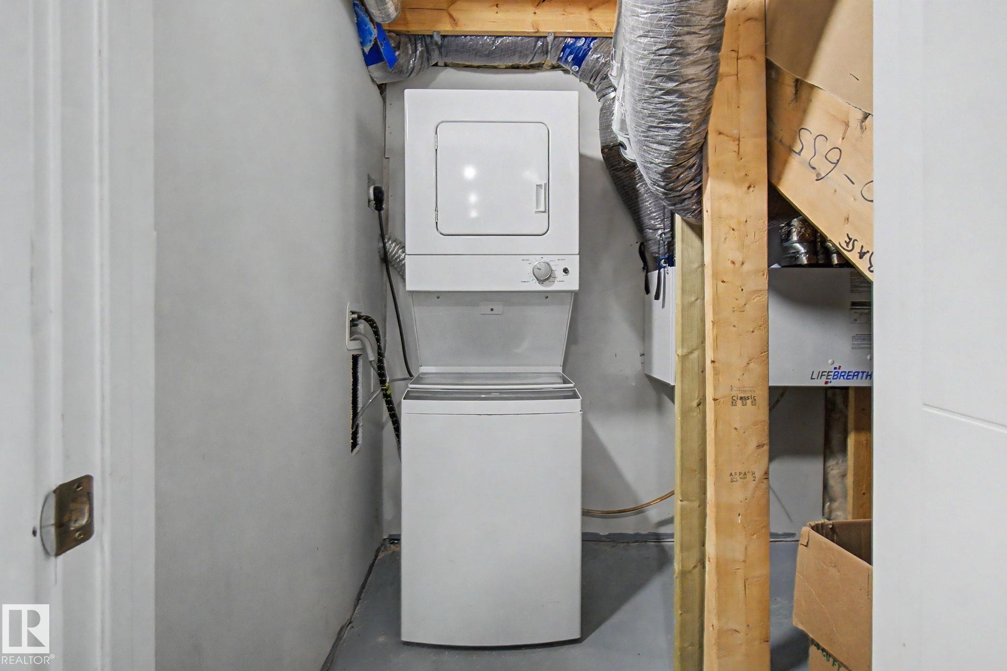 Dedicated laundry area featuring a white stacked washer and dryer unit, exposed wooden beams, and ductwork - 635 42 Street, Edmonton, AB - Indoor Photo Showing Laundry Room