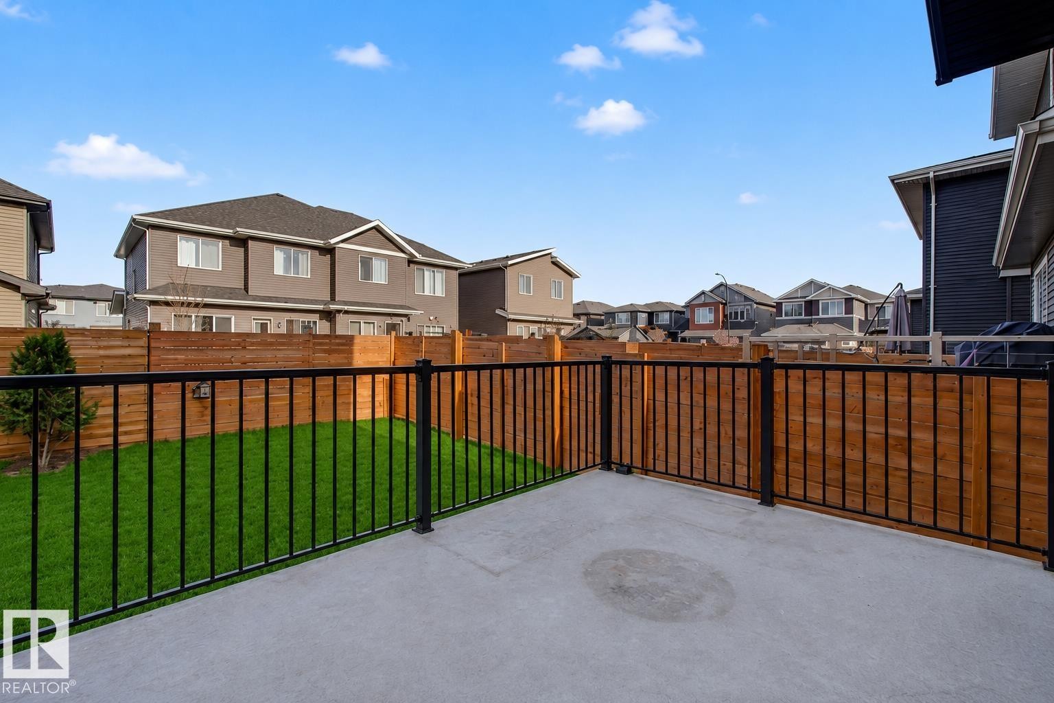 Outdoor concrete patio with black metal railing. Lawn enhanced for summer look. - 635 42 Street, Edmonton, AB - Outdoor With Exterior