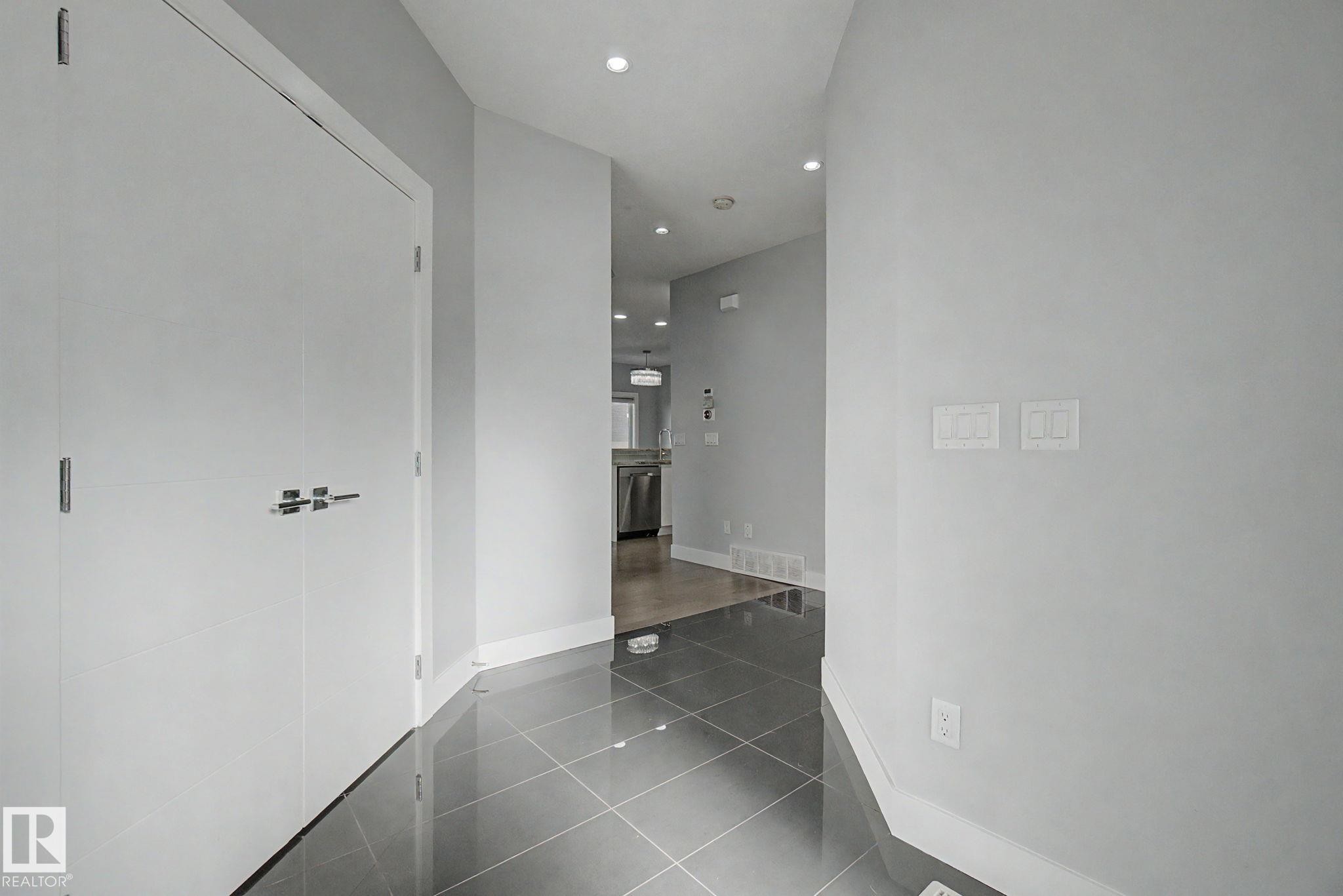 Entryway featuring large format grey tile flooring, white baseboards, recessed ceiling lighting, and two white bi-fold doors with contemporary hardware - 635 42 Street, Edmonton, AB - Indoor Photo Showing Other Room