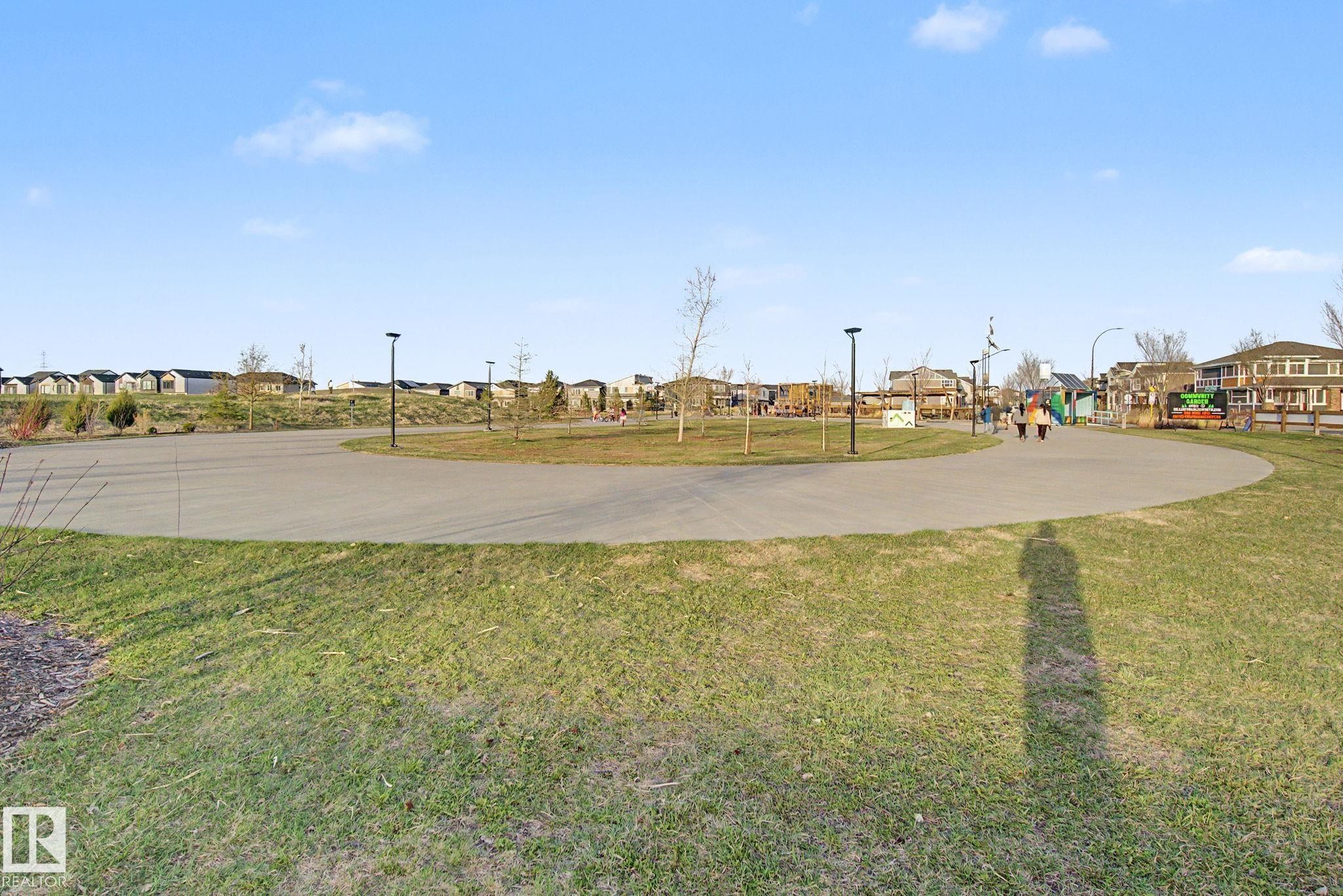 Paved pathway through a green space featuring integrated lighting fixtures, a distant playground structure, and residential architecture bordering the parkland - 635 42 Street, Edmonton, AB - Outdoor With View