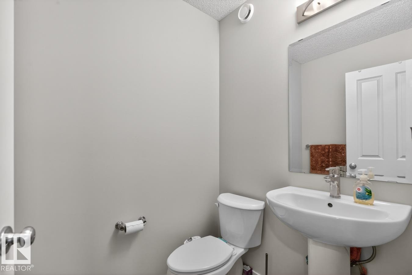Pedestal sink with chrome faucet, wall-mounted mirror, overhead vanity lighting, and white toilet - 3214 9 Street, Edmonton, AB - Indoor Photo Showing Bathroom