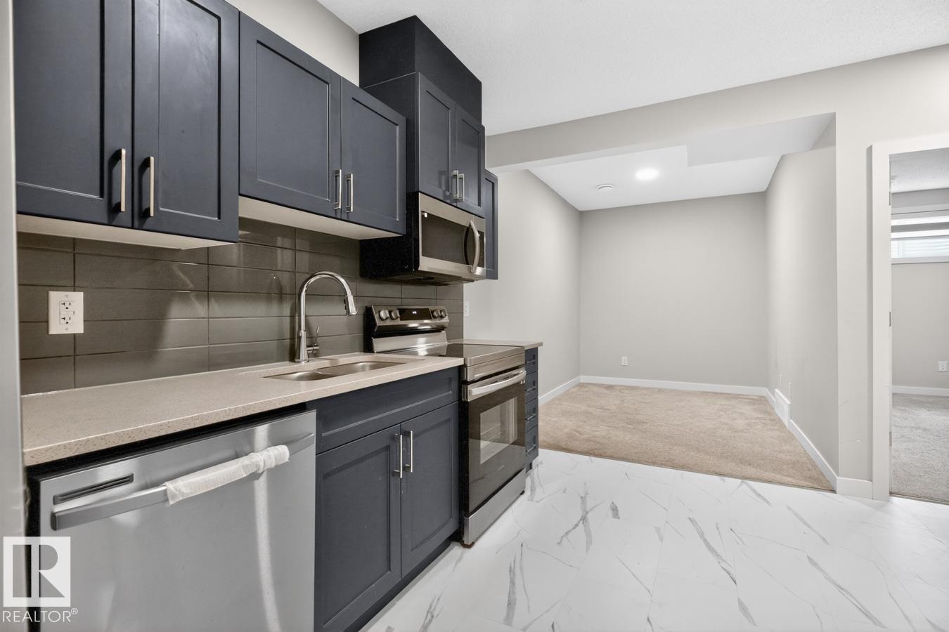 Contemporary kitchen featuring dark cabinetry, stainless steel appliances, a light-toned countertop, and a sleek tile backsplash - 3214 9 Street, Edmonton, AB - Indoor Photo Showing Kitchen With Double Sink