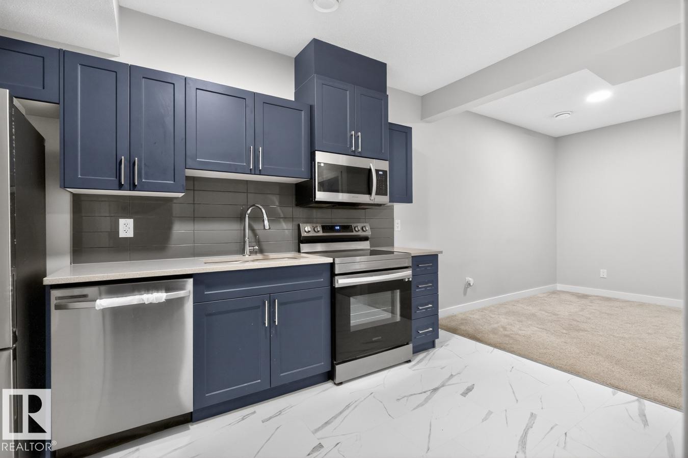 Kitchen featuring blue shaker-style cabinetry, stainless steel appliances, light-colored countertops, and a gray subway tile backsplash - 3214 9 Street, Edmonton, AB - Indoor Photo Showing Kitchen With Stainless Steel Kitchen