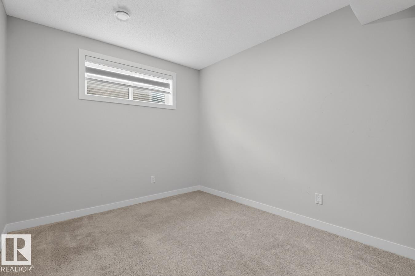 Carpeted room featuring a white-trimmed window with horizontal blinds, light grey wall paint, white baseboards, and a textured white ceiling - 3214 9 Street, Edmonton, AB - Indoor Photo Showing Other Room