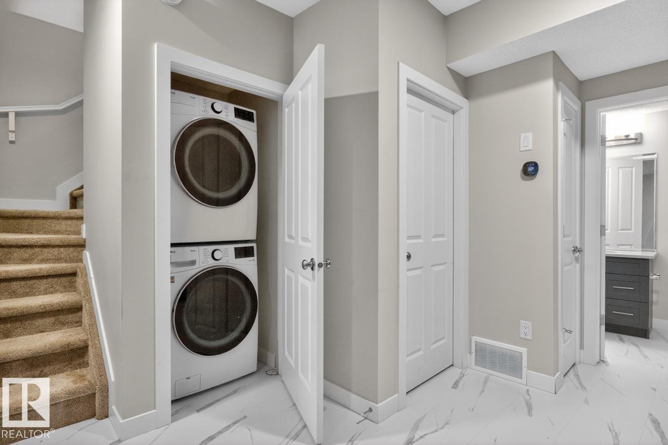 Dedicated laundry area featuring a stacked washer and dryer, adjacent to a carpeted staircase with a wood handrail - 3214 9 Street, Edmonton, AB - Indoor Photo Showing Laundry Room