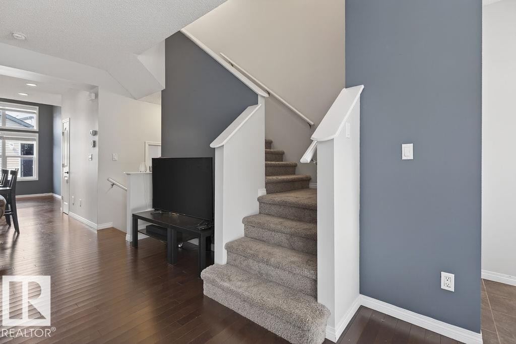 Carpeted staircase with white railings, hardwood-style flooring, and contemporary wall colors - 17540 58 Street Nw, Edmonton, AB