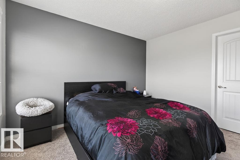 Bedroom featuring a two-tone wall design with a dark accent wall, textured ceiling, light-toned carpet flooring, and a white paneled interior door - 17540 58 Street Nw, Edmonton, AB