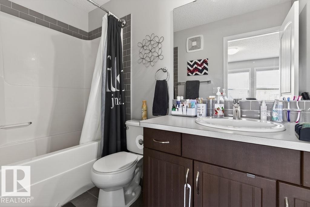 Bathroom featuring a white bathtub, subway tile surround, dark wood-finish vanity with a light countertop, and a built-in mirror - 17540 58 Street Nw, Edmonton, AB