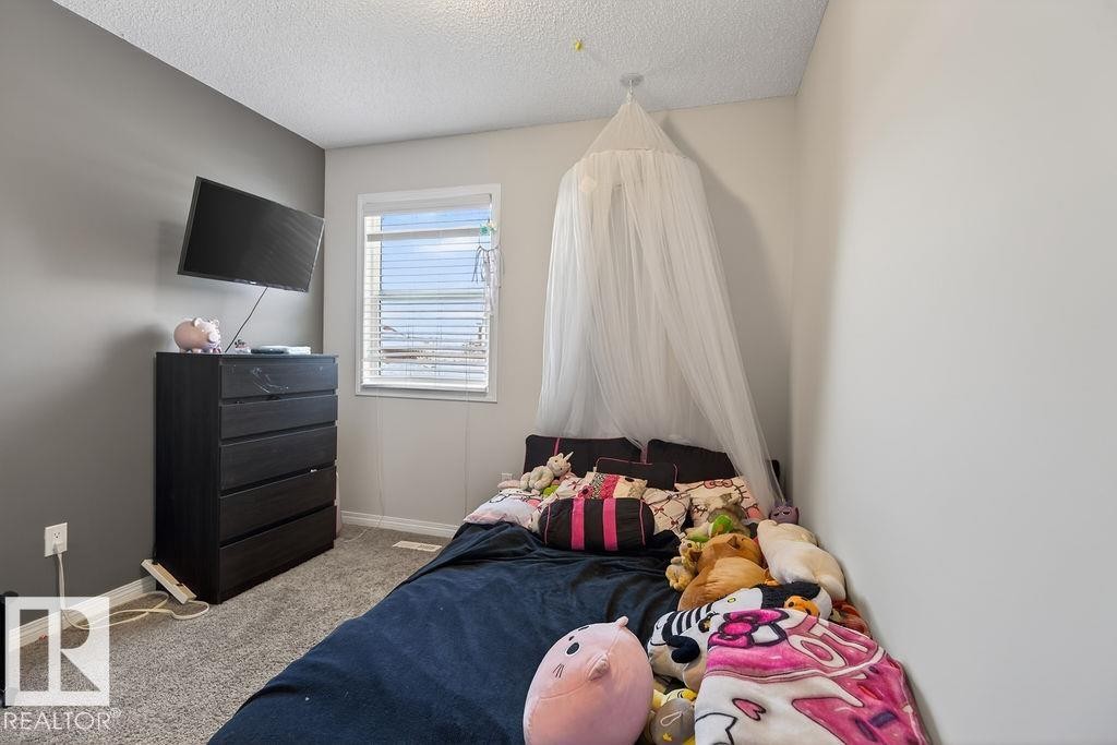 Carpeted room featuring a single window with horizontal blinds, a textured ceiling, and a paneled accent wall - 17540 58 Street Nw, Edmonton, AB