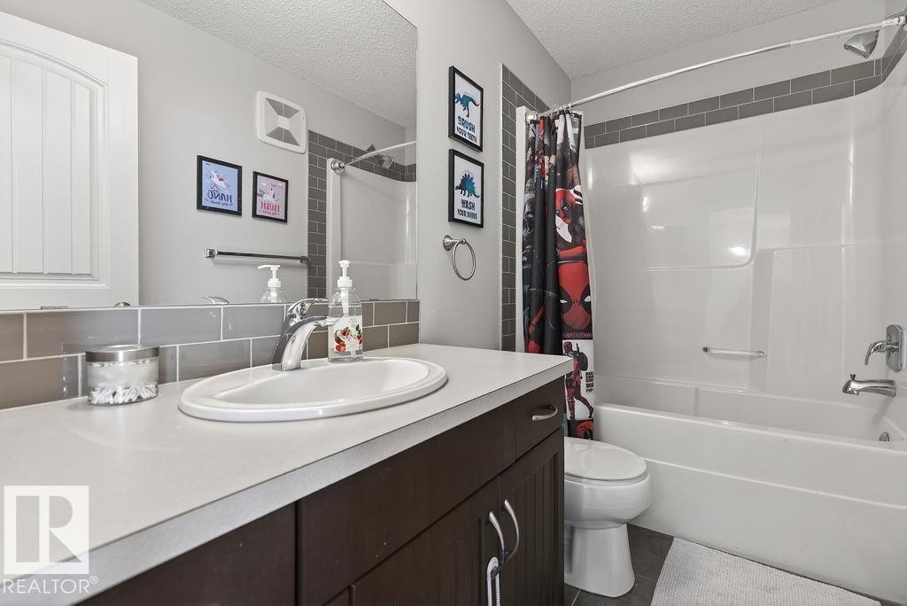 Bathroom featuring a built-in vanity with a composite countertop and integrated sink, a large wall-mounted mirror, and a full-size bathtub with a shower - 17540 58 Street Nw, Edmonton, AB