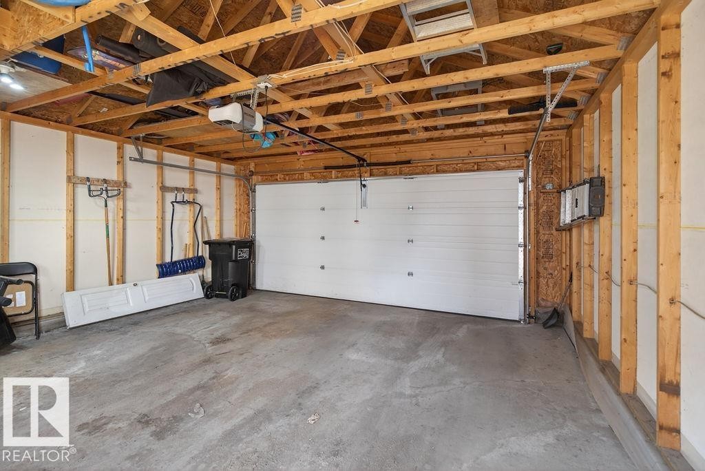 Spacious garage featuring a concrete floor, exposed wood framing, and a white overhead garage door with an automatic opener - 17540 58 Street Nw, Edmonton, AB