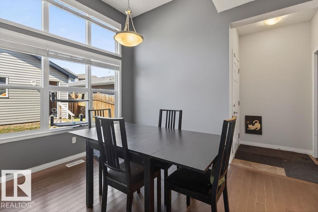 Dining area featuring wood-finish flooring, a large window with transom, and a ceiling-mounted light fixture - 17540 58 Street Nw, Edmonton, AB