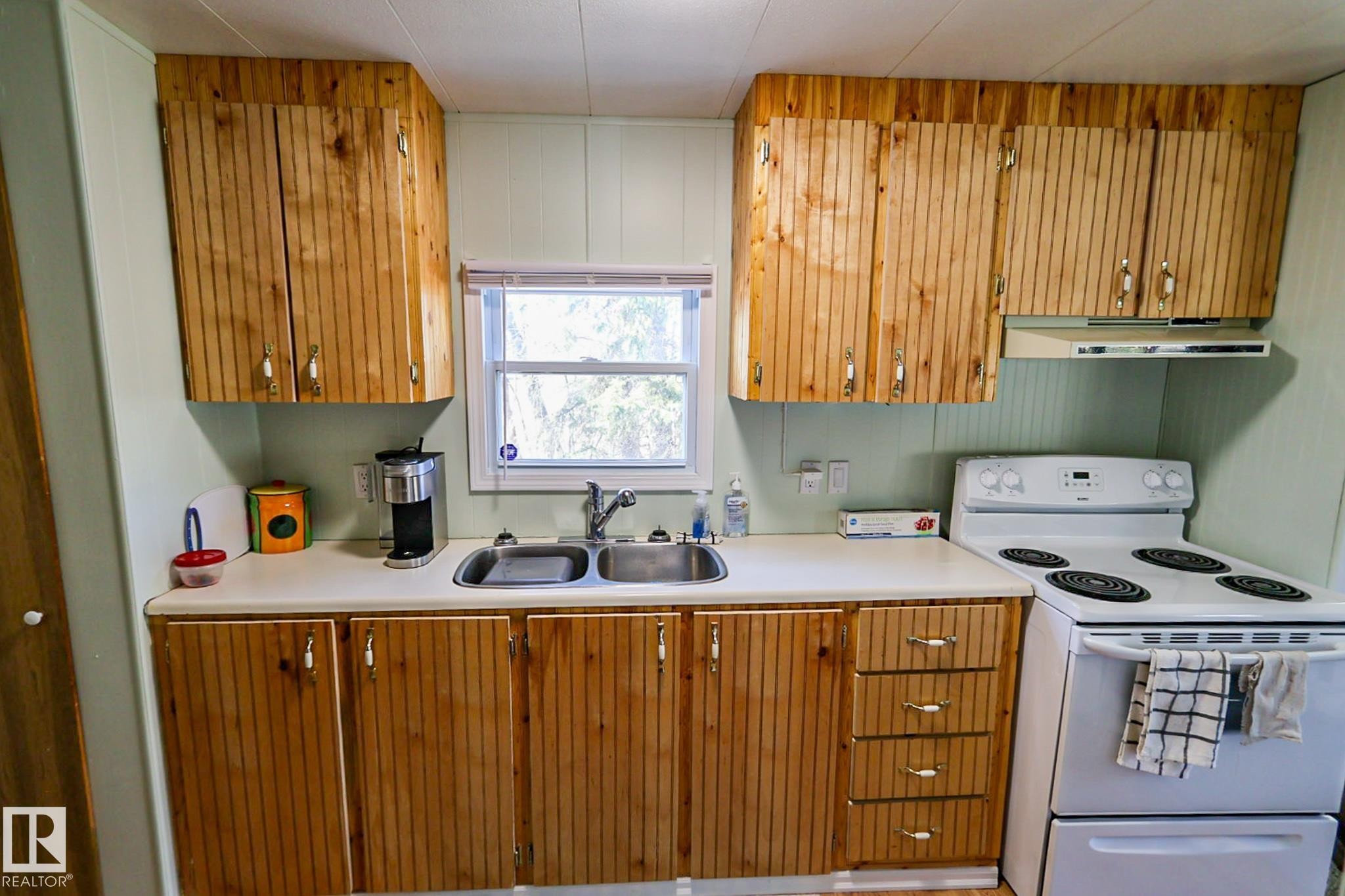 Kitchen featuring natural wood cabinetry, light countertops, a stainless steel double basin sink, and a four-burner electric range - 331 60417 Range Road 124, Rural St. Paul County, AB