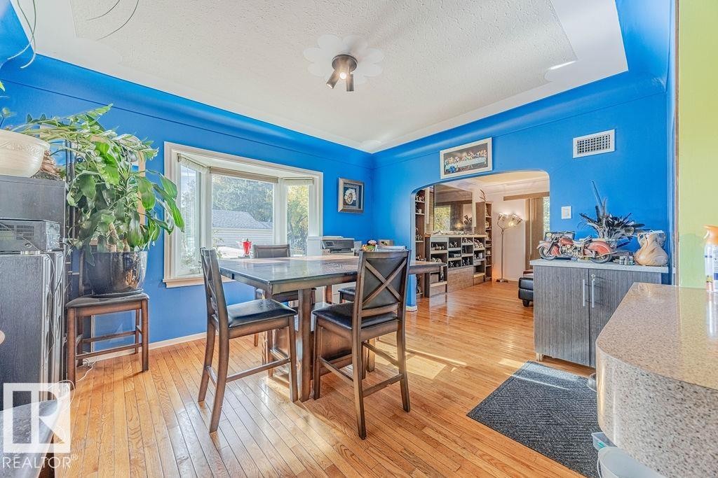 Hardwood flooring throughout featuring a bay window, a built-in archway, and a ceiling light fixture - 12339 89 Street, Edmonton, AB - Indoor Photo Showing Dining Room