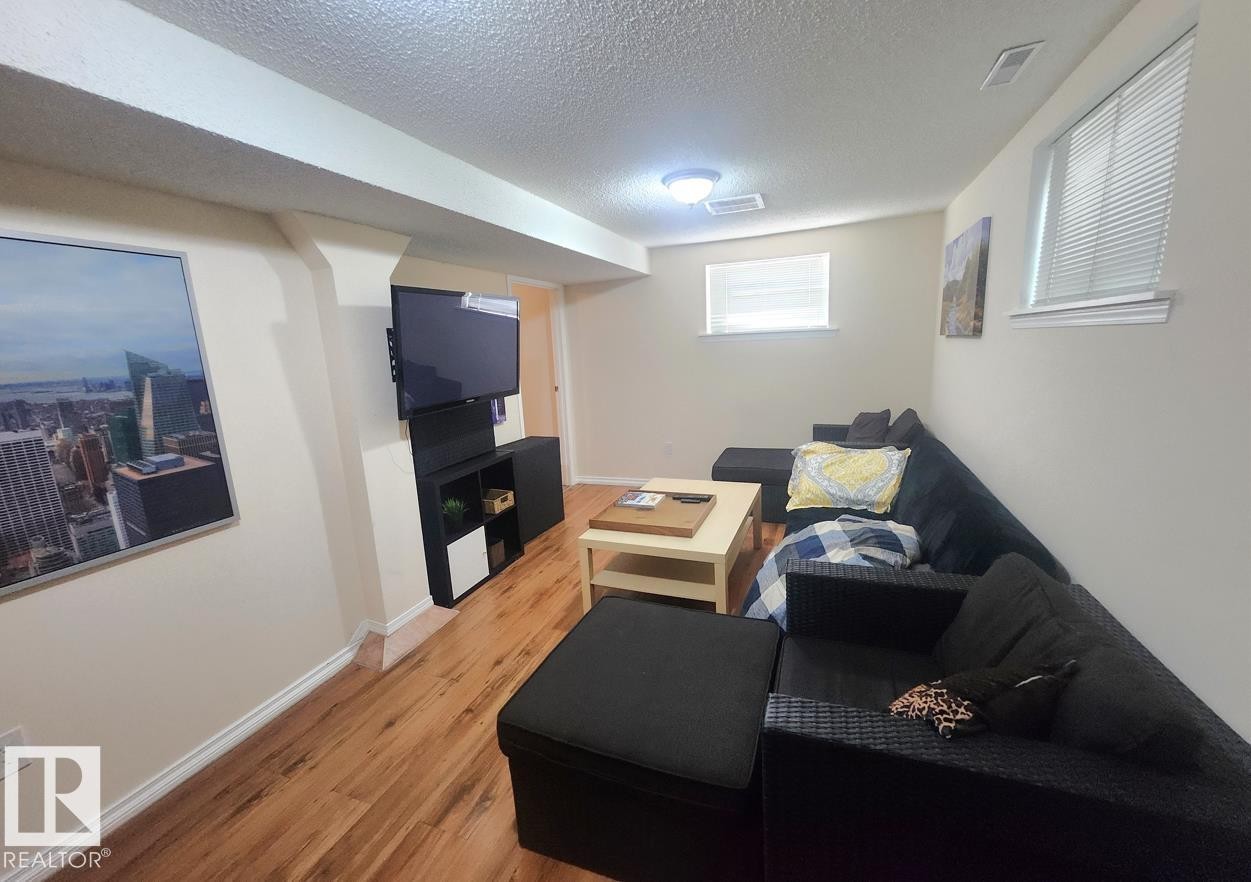 Wood-finish flooring throughout this room featuring multiple windows with blinds, a ceiling-mounted light fixture, and a built-in wall niche - 12339 89 Street, Edmonton, AB - Indoor