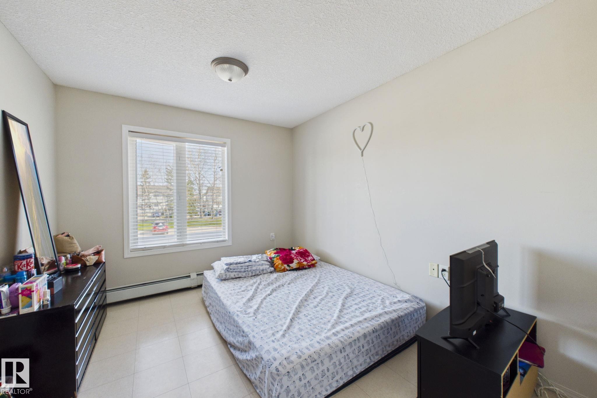 Neutral wall paint, textured ceiling, and a large window with blinds - 220 80A Kelloway Crescent, Red Deer, AB - Indoor Photo Showing Bedroom