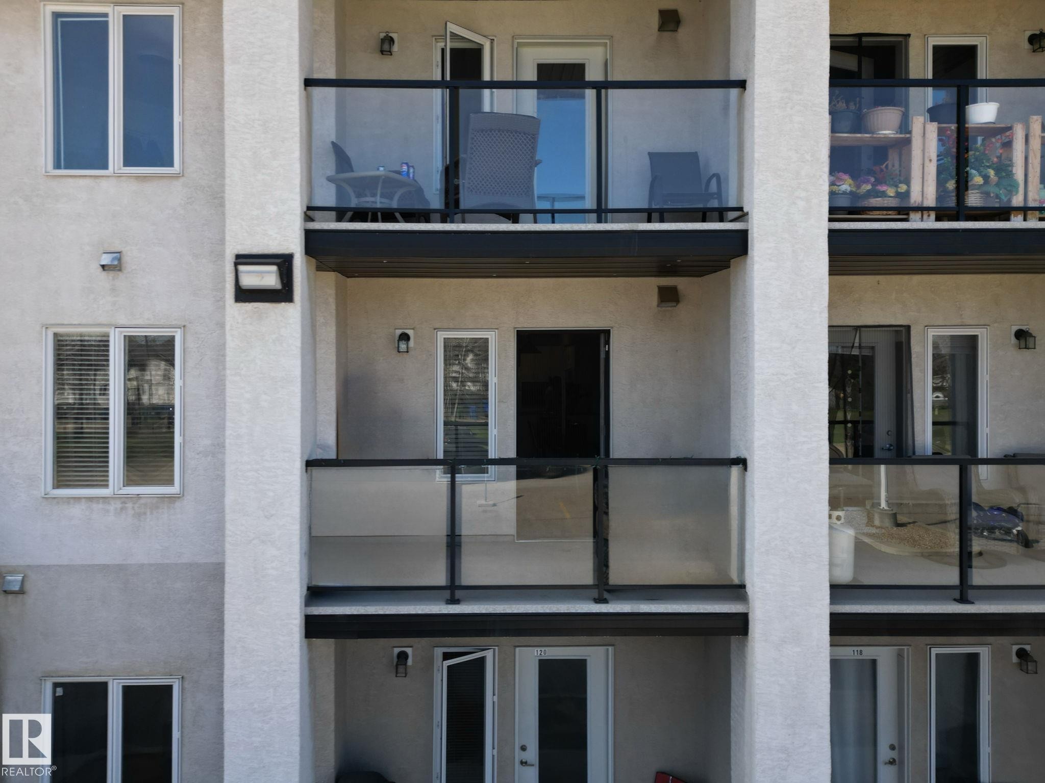Multi-story building facade featuring textured exterior finish and multiple private balconies with glass and black metal railings - 220 80A Kelloway Crescent, Red Deer, AB - Outdoor With Balcony