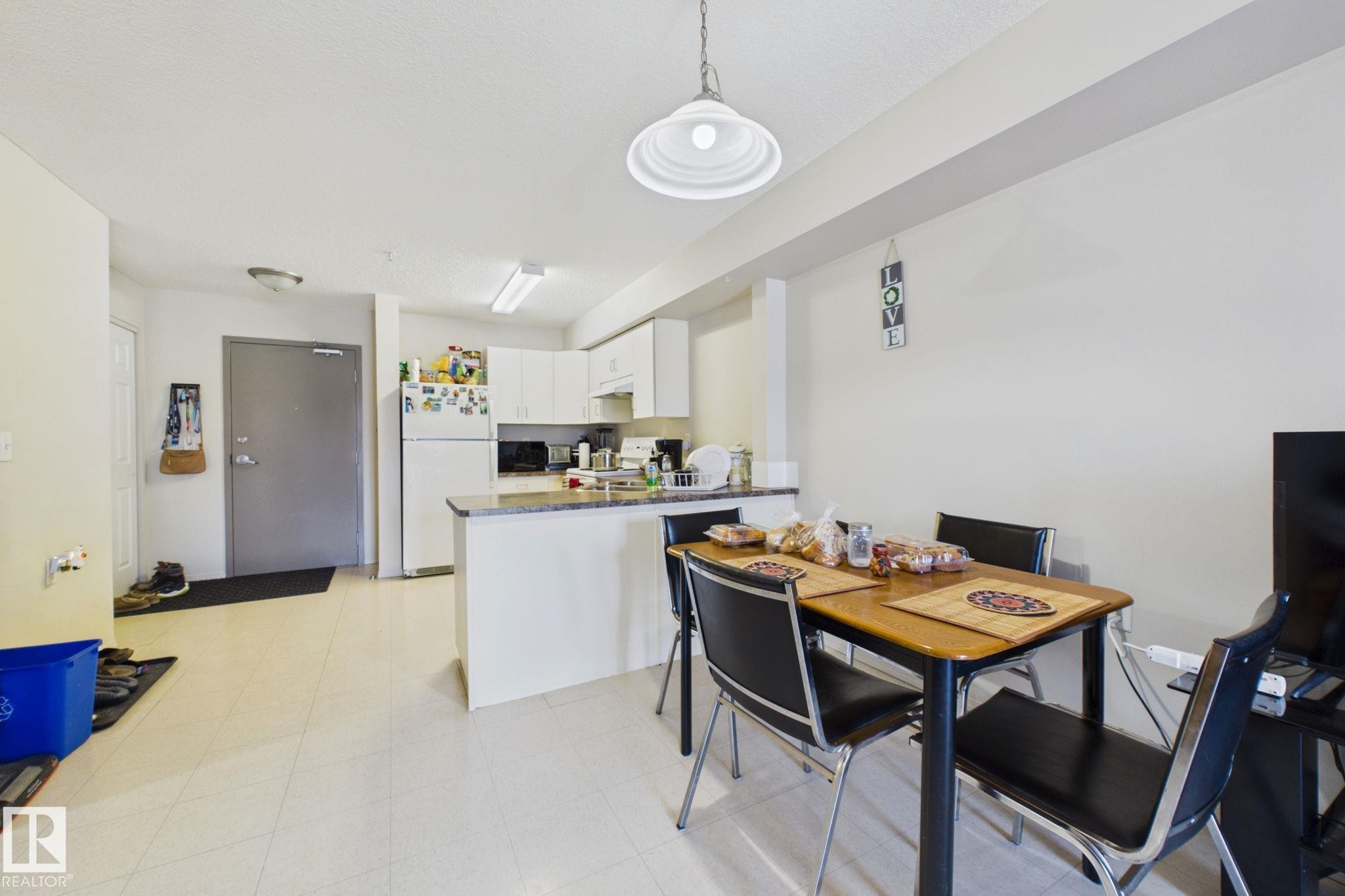 Open-concept living area featuring light-toned flooring, a kitchen with white cabinetry and a built-in breakfast bar, and a dining area - 220 80A Kelloway Crescent, Red Deer, AB - Indoor