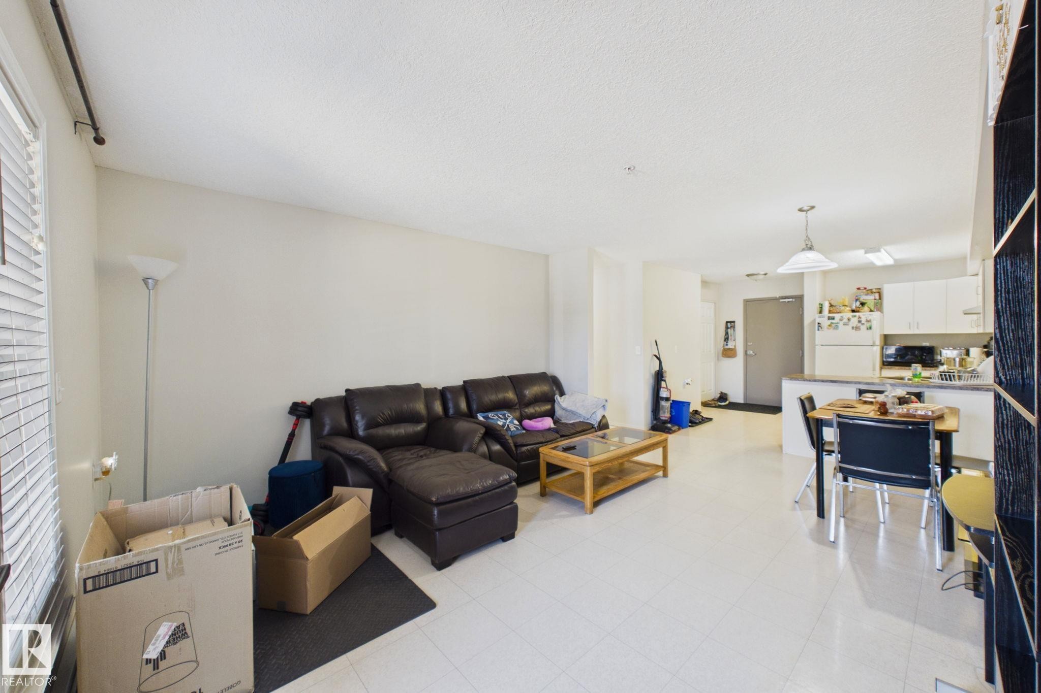 Open-concept living space featuring light-toned flooring, white walls, and a visible kitchen area with white cabinetry and dark countertops - 220 80A Kelloway Crescent, Red Deer, AB - Indoor