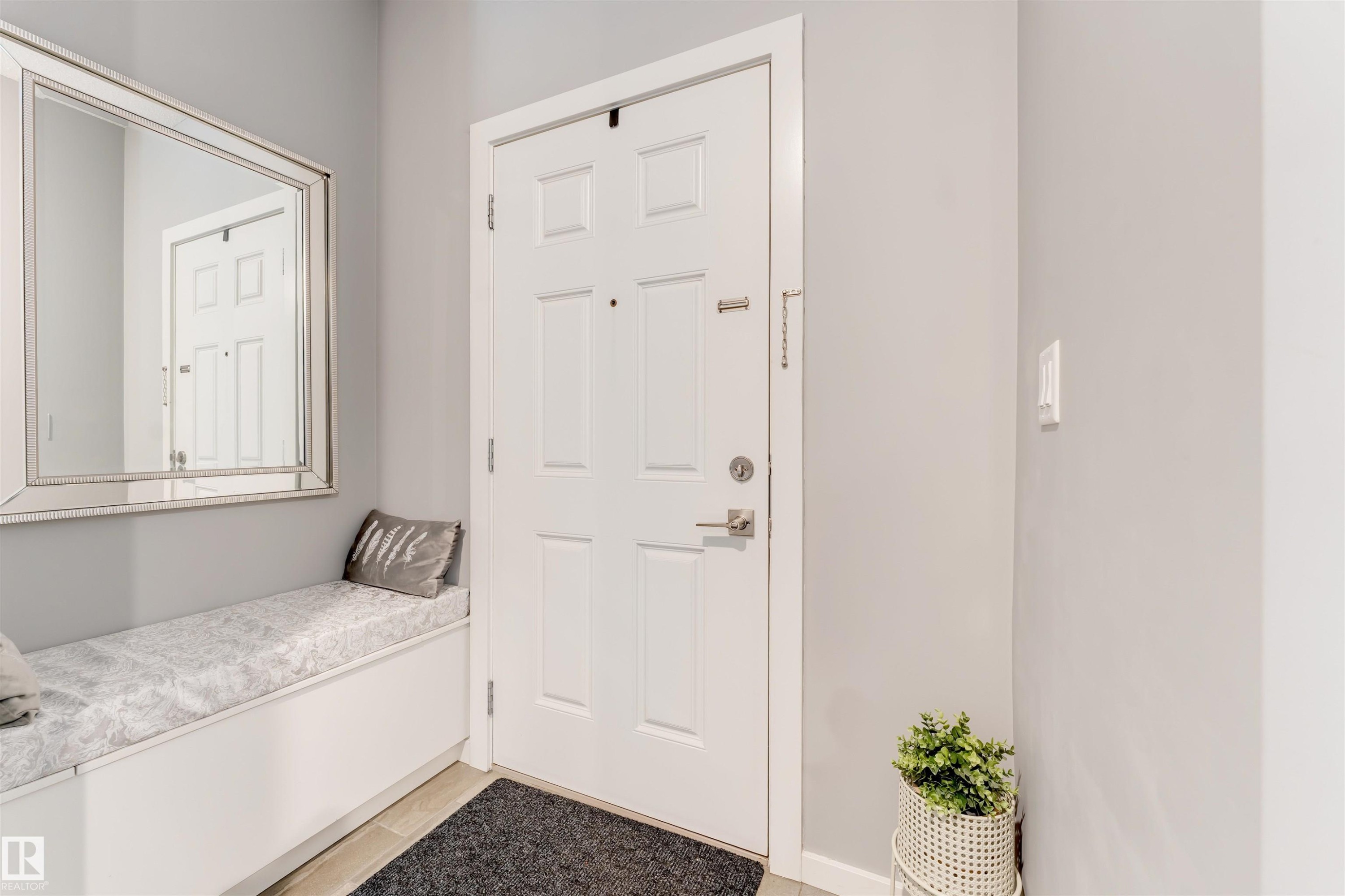 Entryway featuring a paneled door with brushed nickel hardware, light gray walls, built-in bench seating with a cushion, and a large framed mirror - 2652 Maple Way, Edmonton, AB - Indoor Photo Showing Other Room