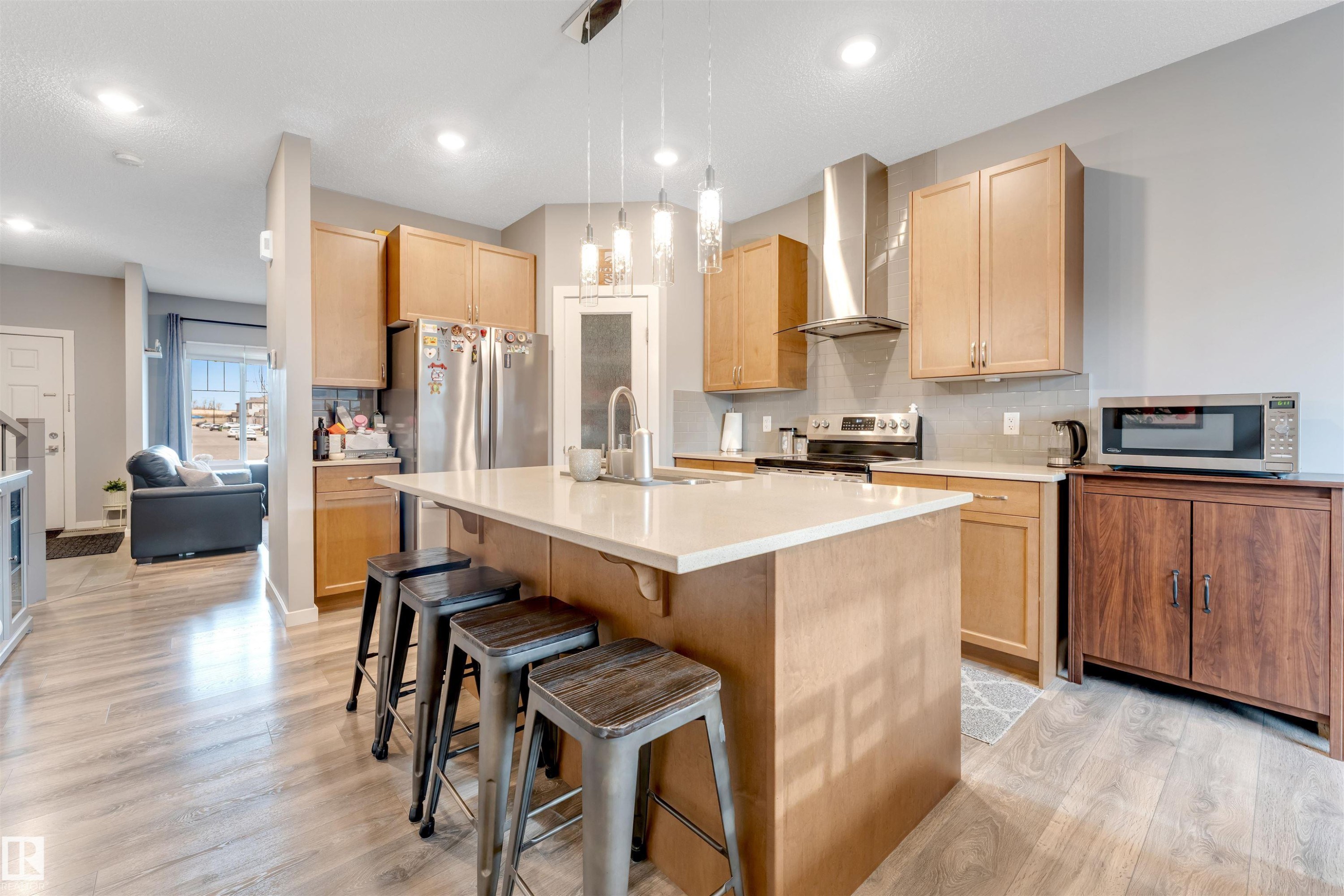 Modern kitchen featuring an expansive center island with seating, pendant lighting, stainless steel appliances, light wood-finish cabinetry, and wood-finish flooring - 2652 Maple Way, Edmonton, AB - Indoor Photo Showing Kitchen With Upgraded Kitchen