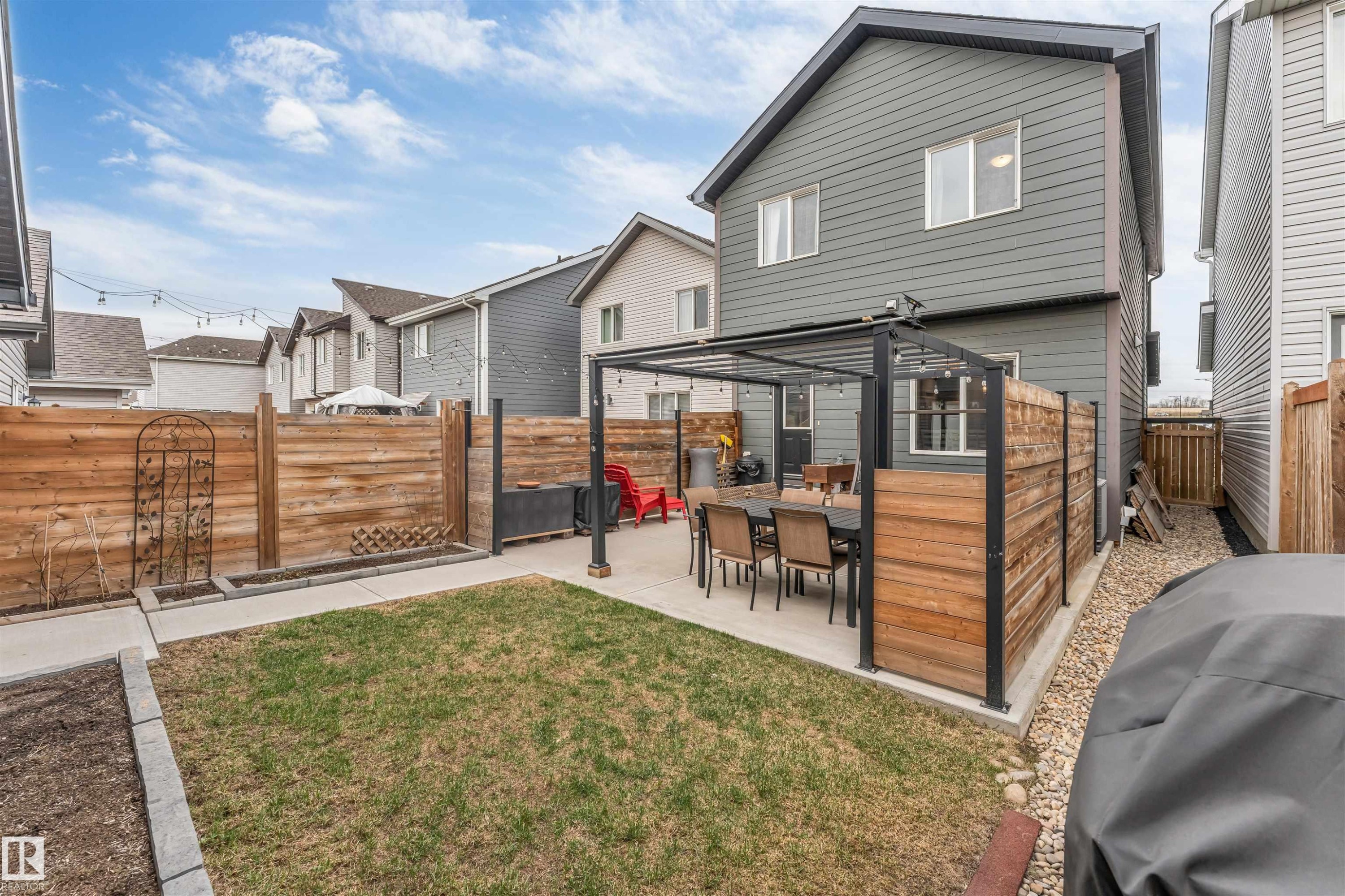 Private backyard featuring a concrete patio with a built-in pergola, horizontal wood fencing, a grass lawn, and a side yard with gravel - 2652 Maple Way, Edmonton, AB - Outdoor With Deck Patio Veranda With Exterior