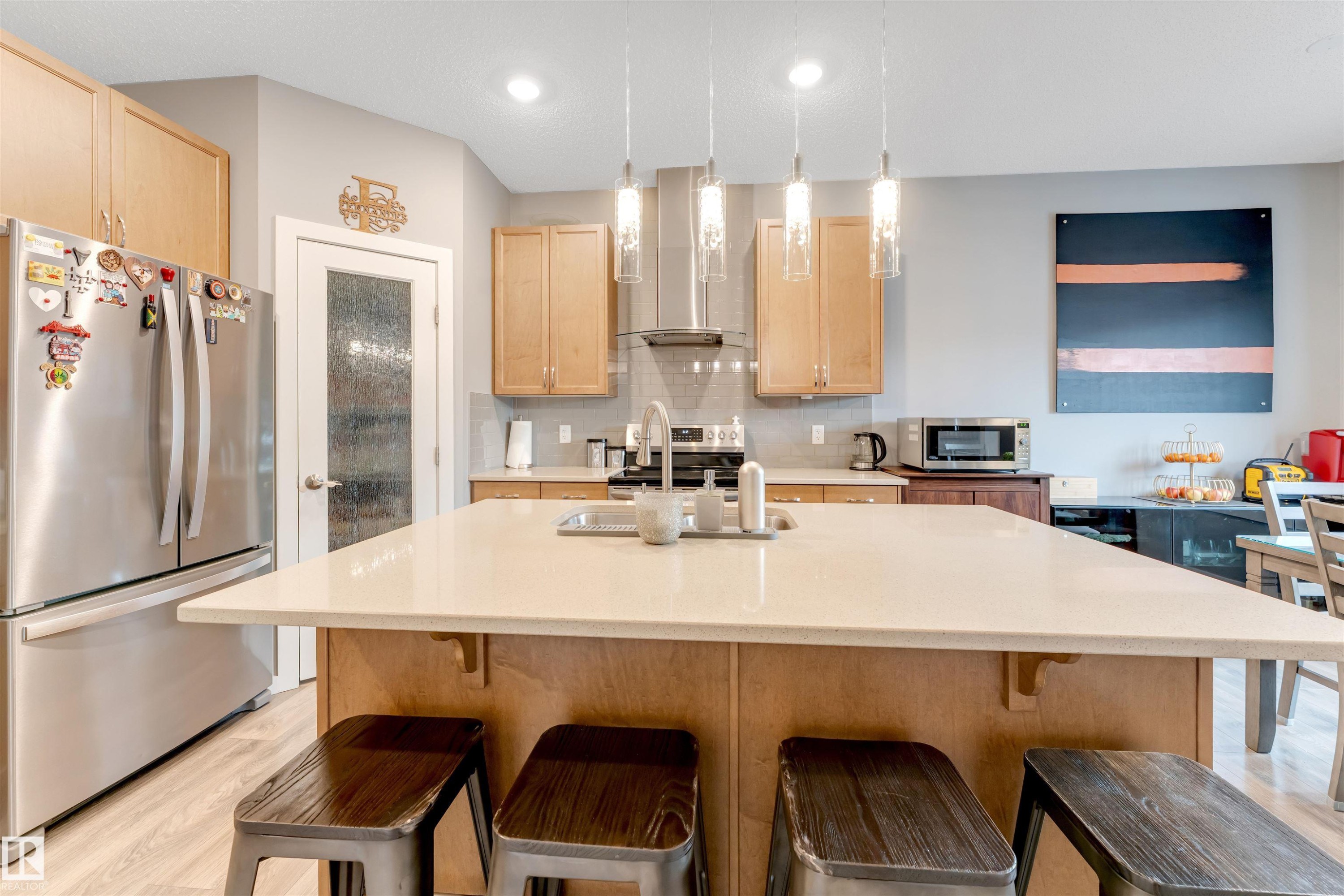 Spacious kitchen featuring a large central island with light-toned countertop, stainless steel appliances, wood-finish cabinetry, and recessed lighting - 2652 Maple Way, Edmonton, AB - Indoor Photo Showing Kitchen With Upgraded Kitchen