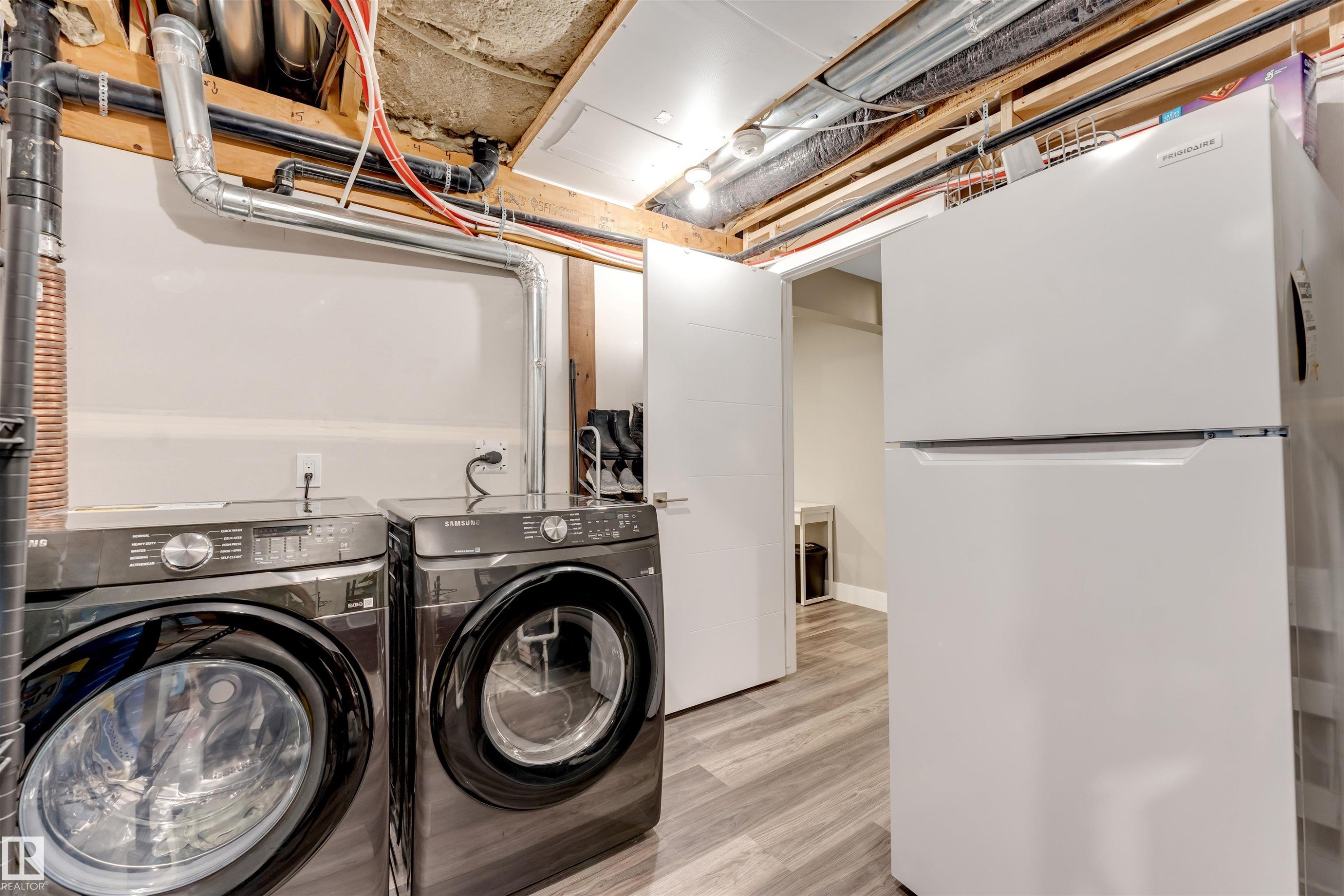 Dedicated laundry area featuring a front-loading washer and dryer set, wood-finish flooring, and a full-size refrigerator - 2652 Maple Way, Edmonton, AB - Indoor Photo Showing Laundry Room