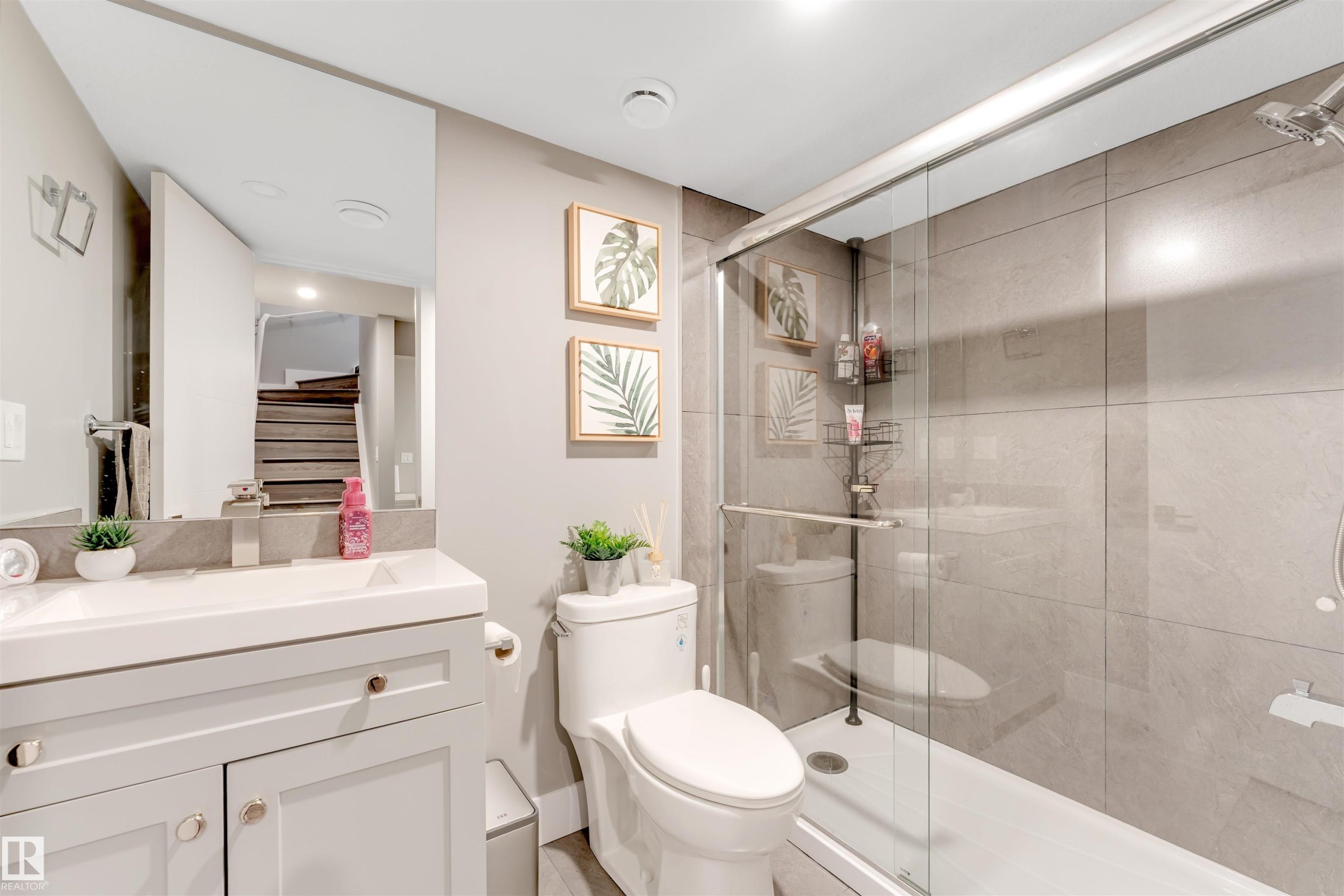 Bathroom featuring a glass-enclosed shower with tile surround, a single vanity with a white countertop and undermount sink, a wall-mounted mirror, and a toilet - 2652 Maple Way, Edmonton, AB - Indoor Photo Showing Bathroom