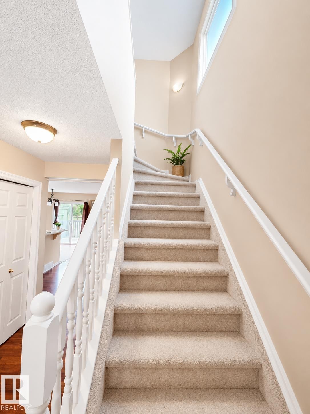 Carpeted staircase with white balusters and handrails, featuring a high transom window, two wall sconces, and a flush mount ceiling light - 704 83 Street, Edmonton, AB - Indoor Photo Showing Other Room