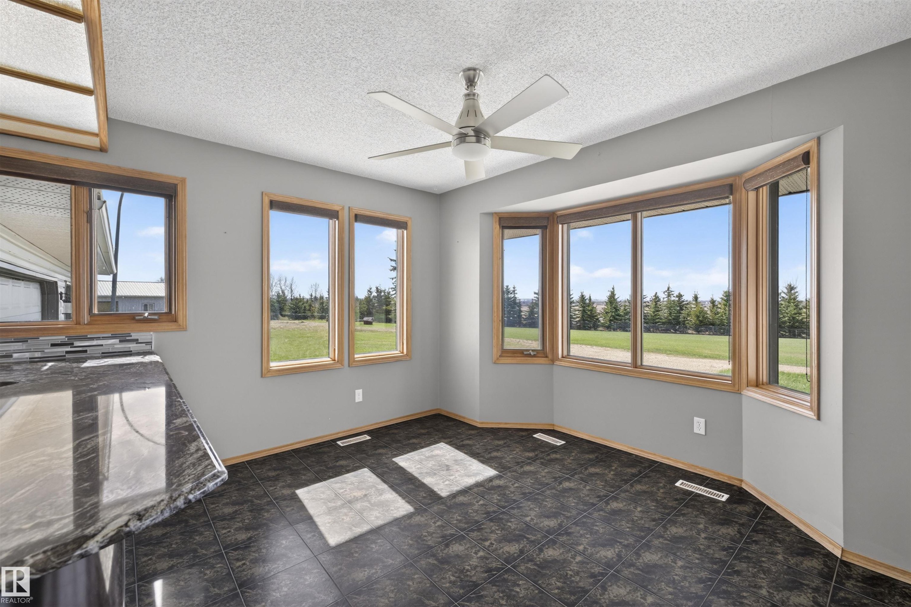 Bay window with natural wood trim, contemporary ceiling fan, dark tile flooring, and light gray walls - 19403 Fort Road, Edmonton, AB - Indoor Photo Showing Other Room