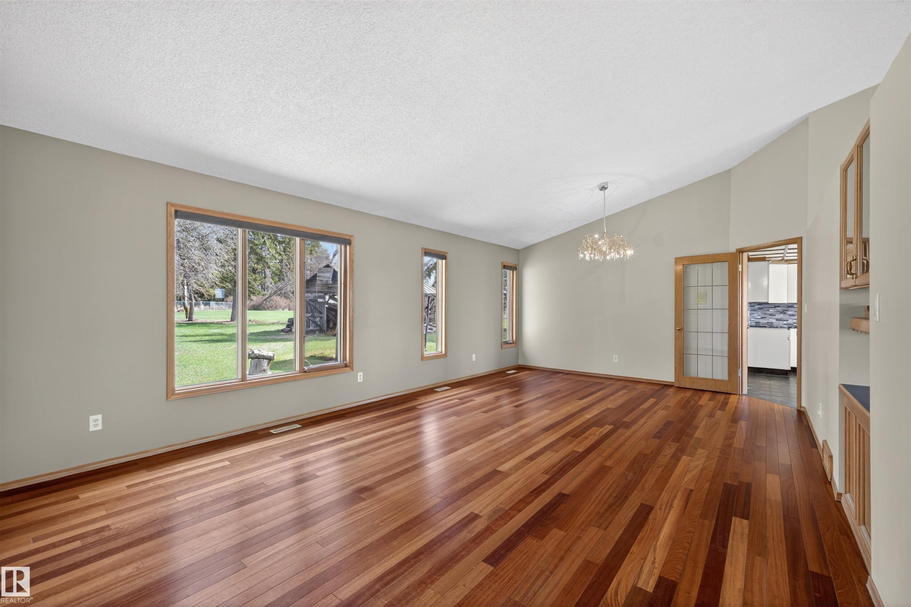 Spacious interior featuring wood-finish flooring, multiple windows, a decorative chandelier, and vaulted ceilings - 19403 Fort Road, Edmonton, AB - Indoor Photo Showing Other Room