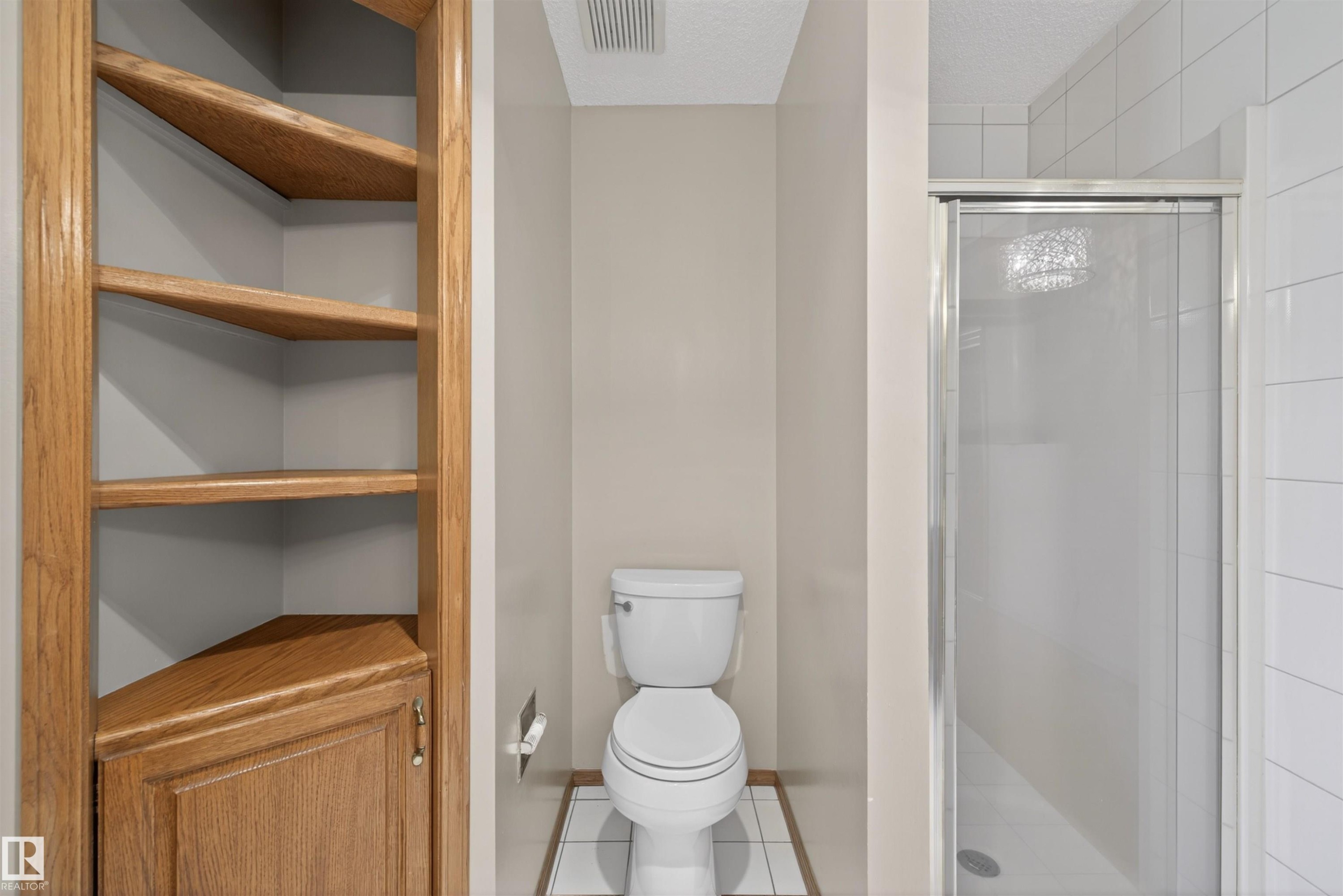 Corner built-in shelving with a lower cabinet, a toilet, and a glass-enclosed shower with white tiled walls - 19403 Fort Road, Edmonton, AB - Indoor Photo Showing Bathroom