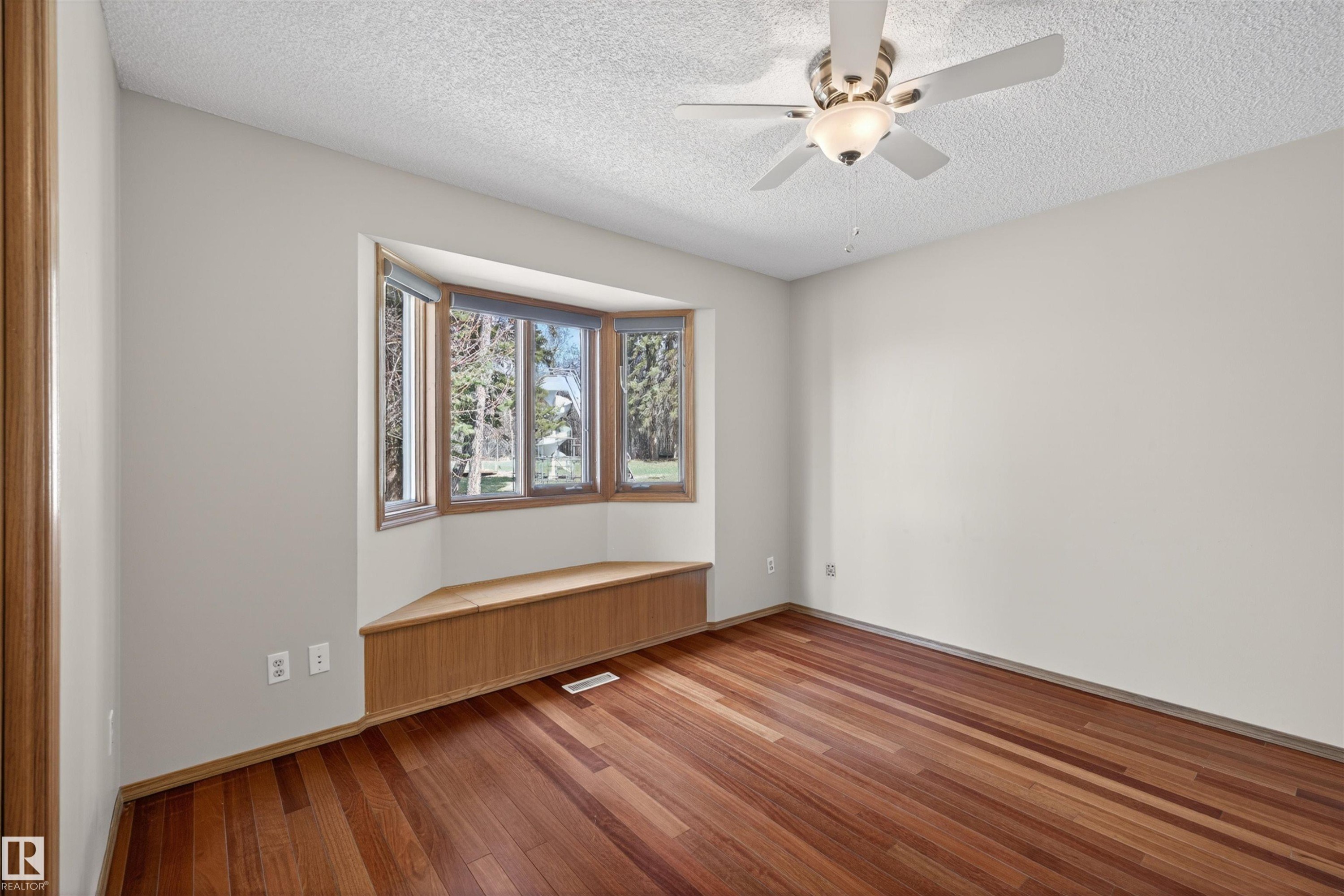 Bay window with a built-in window seat, wood-finish flooring, textured ceiling, and a ceiling fan with integrated lighting - 19403 Fort Road, Edmonton, AB - Indoor Photo Showing Other Room