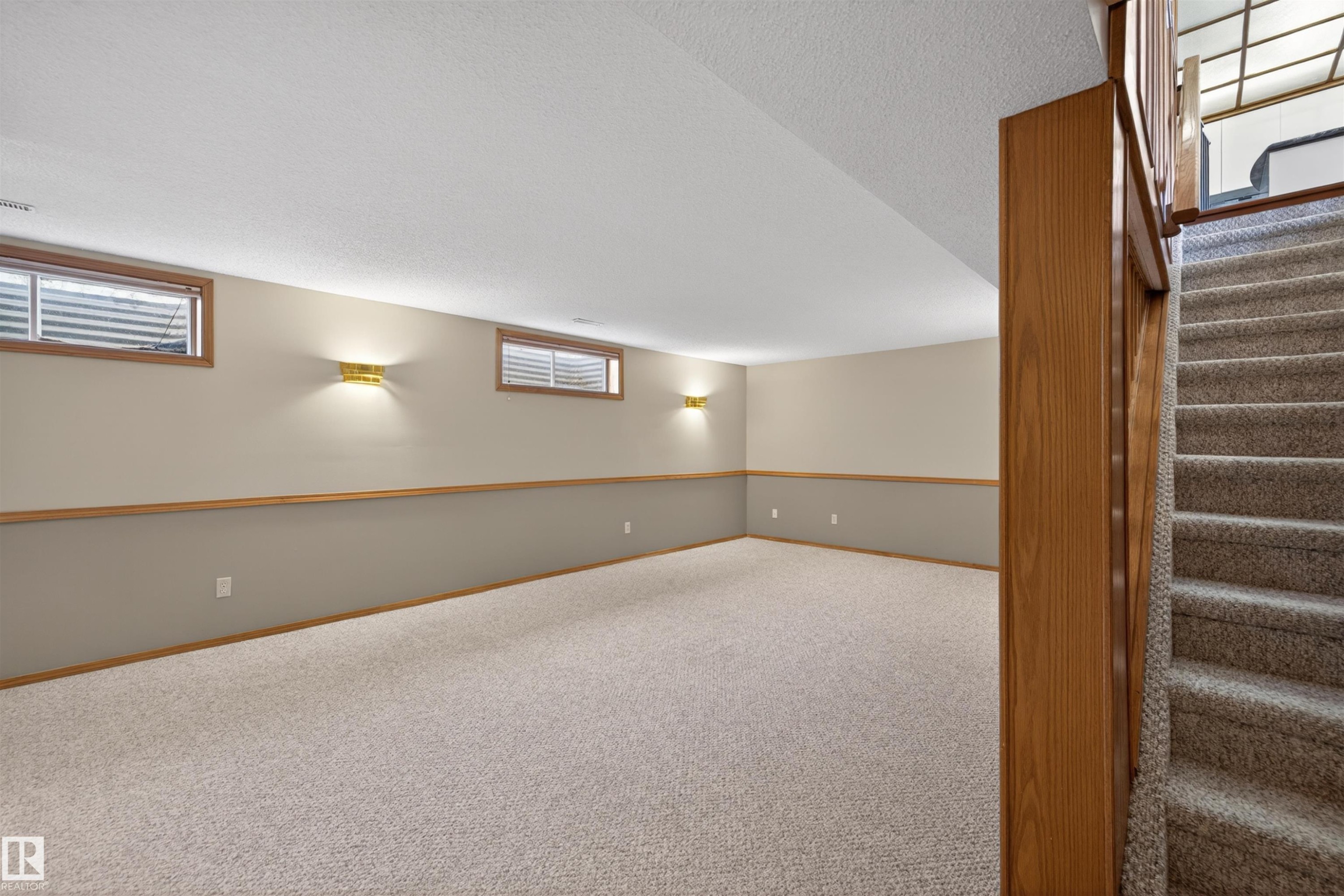 Spacious lower-level room featuring light carpet, two-tone painted walls with wood trim, and wood-framed windows - 19403 Fort Road, Edmonton, AB - Indoor Photo Showing Other Room