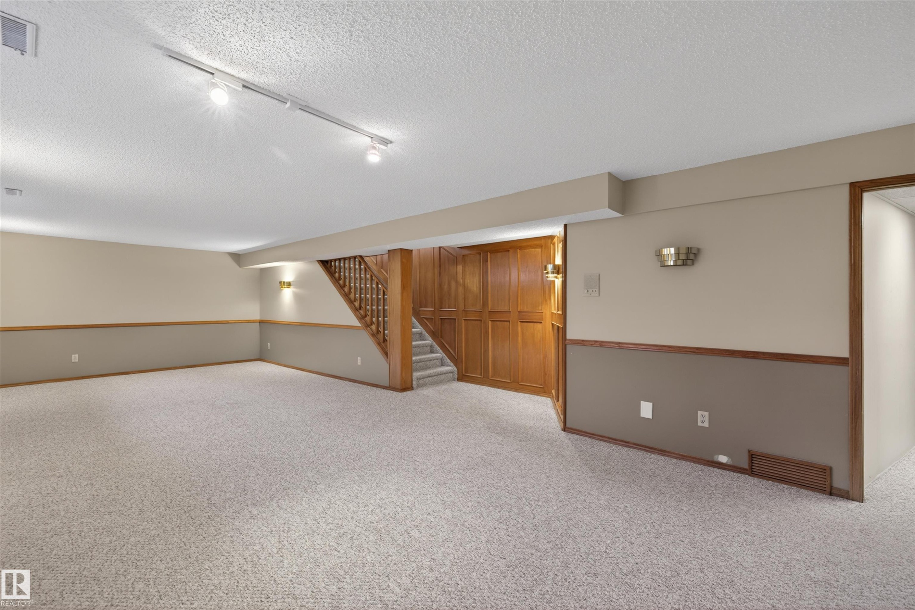 Spacious lower level featuring light-toned carpeting, a wood staircase with balusters, and track lighting - 19403 Fort Road, Edmonton, AB - Indoor Photo Showing Other Room
