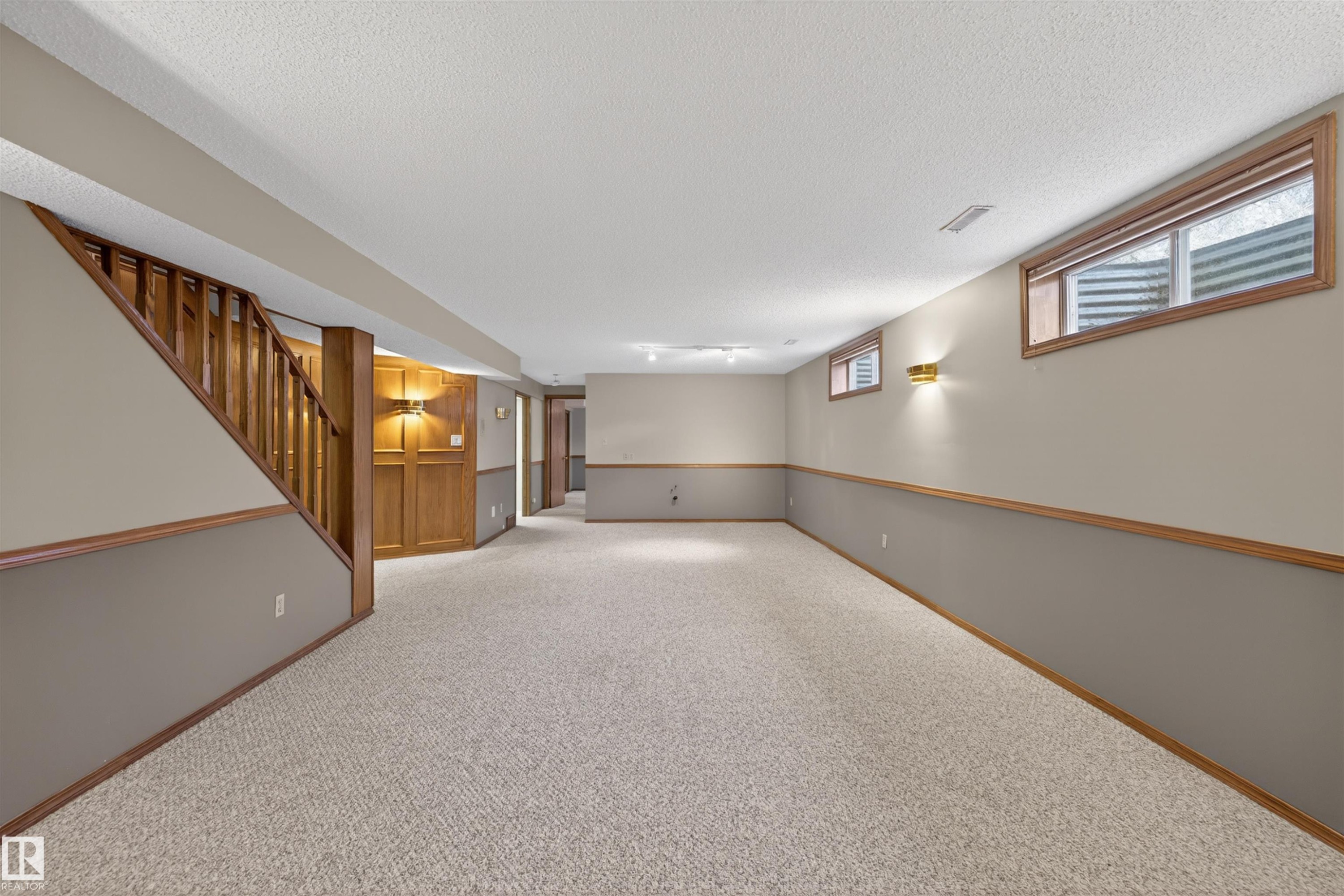 Expansive carpeted room featuring a wooden staircase and paneling - 19403 Fort Road, Edmonton, AB - Indoor Photo Showing Other Room