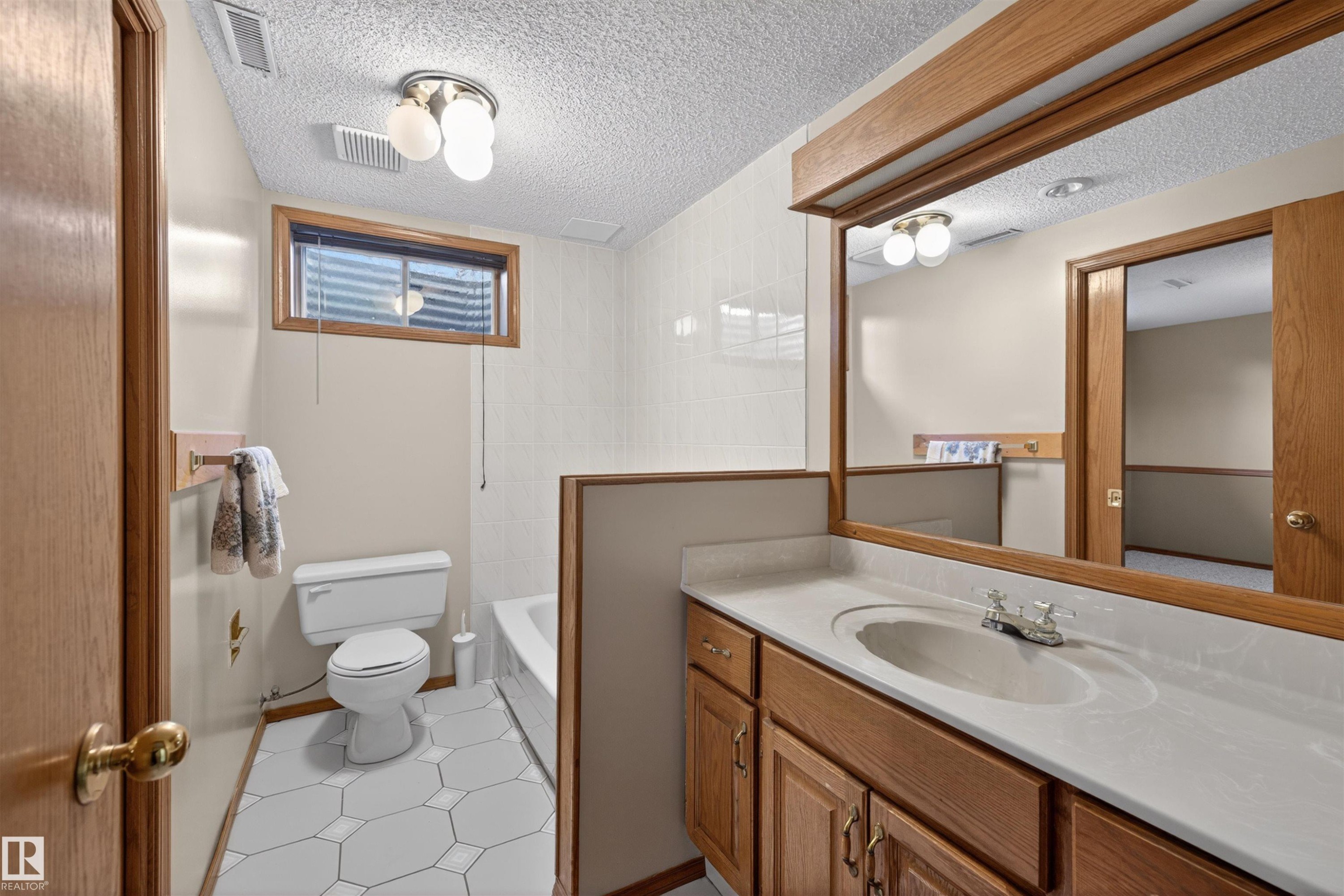 Bathroom featuring a single vanity with a white countertop and integrated sink, wood-finish cabinetry, a framed wall mirror, and hexagonal floor tiling - 19403 Fort Road, Edmonton, AB - Indoor Photo Showing Bathroom