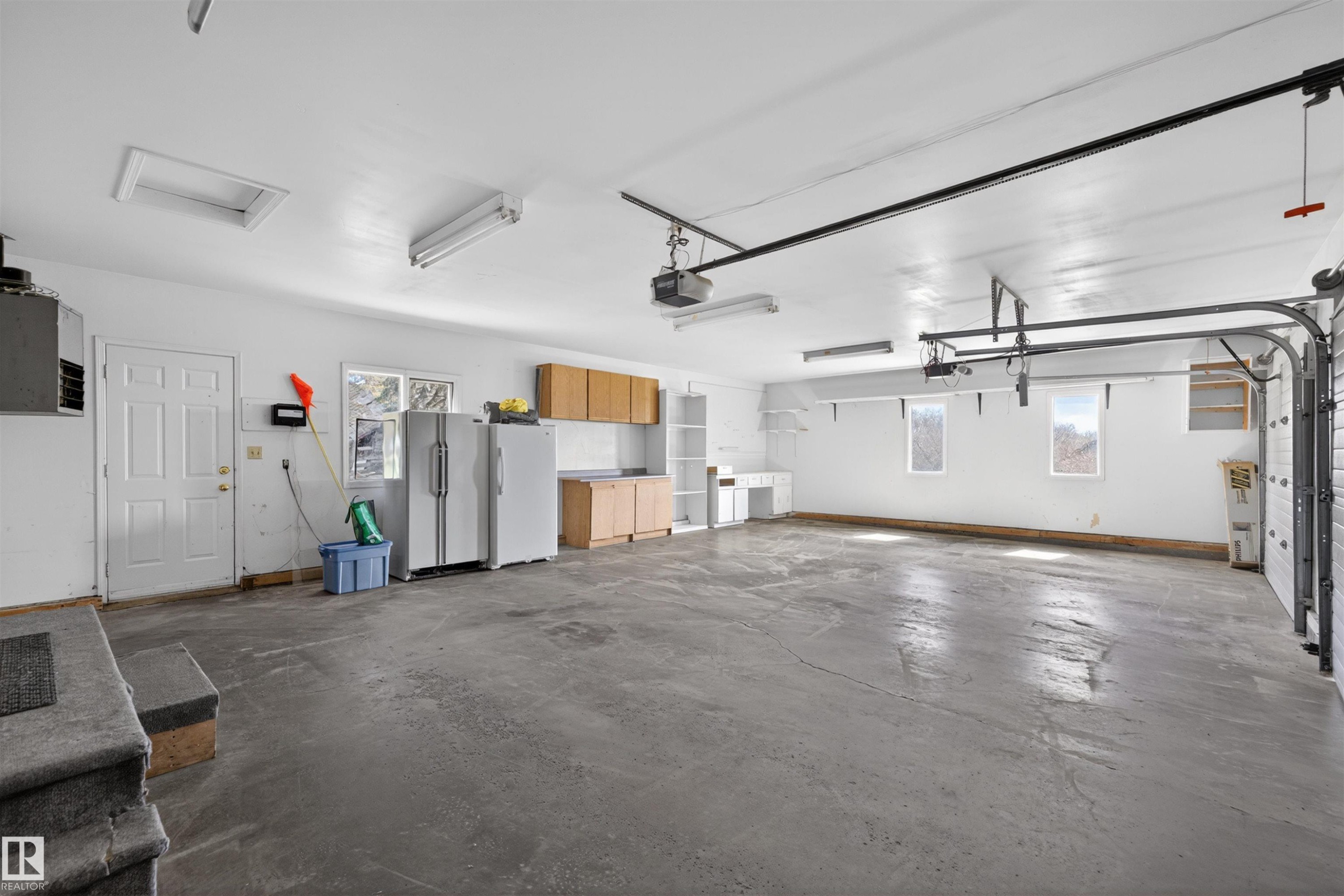 Spacious garage featuring a concrete floor, multiple windows, built-in cabinetry, and overhead lighting - 19403 Fort Road, Edmonton, AB - Indoor Photo Showing Garage