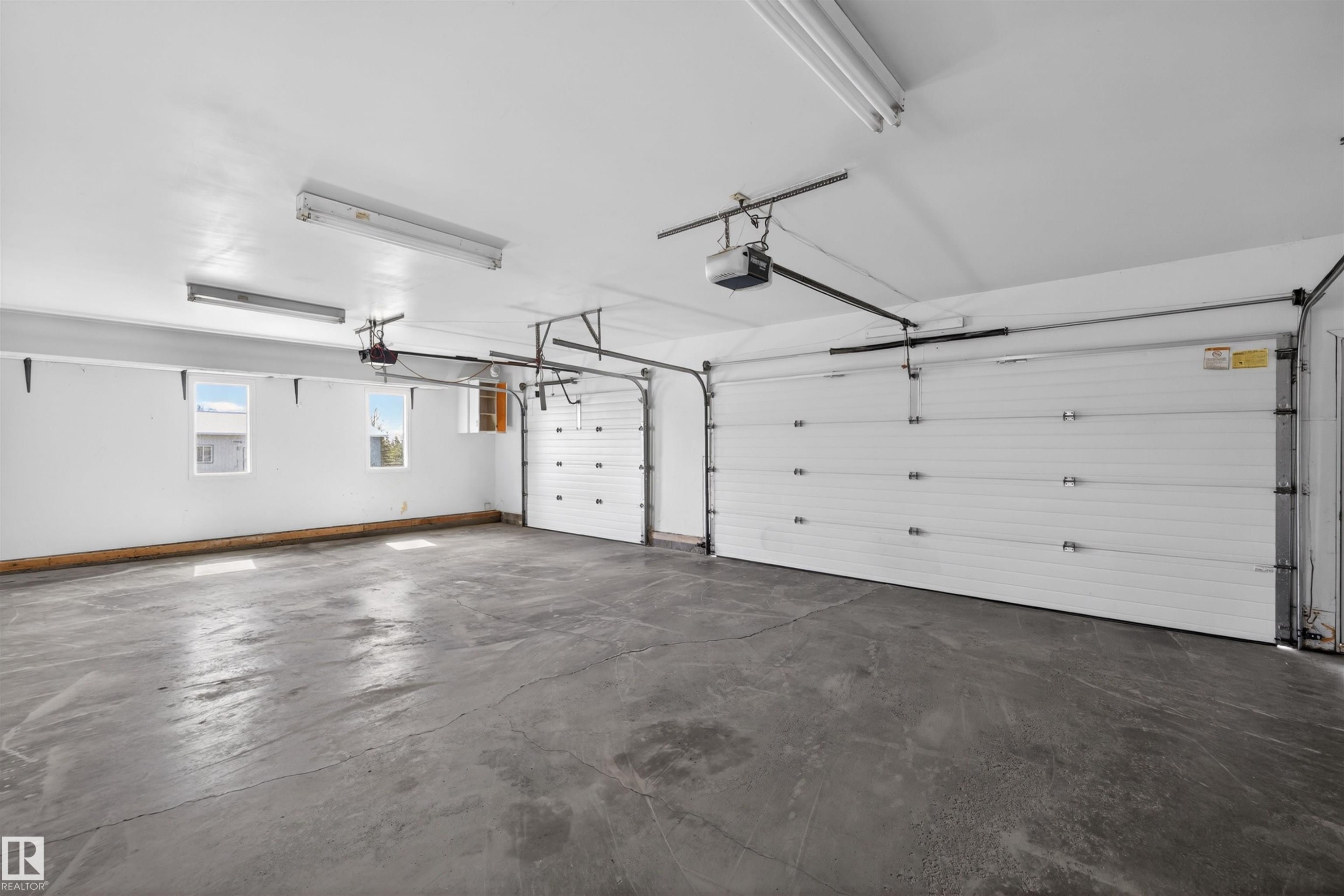 Spacious garage featuring two overhead doors with automatic openers, a durable concrete floor, multiple windows providing natural light, and fluorescent overhead lighting - 19403 Fort Road, Edmonton, AB - Indoor Photo Showing Garage