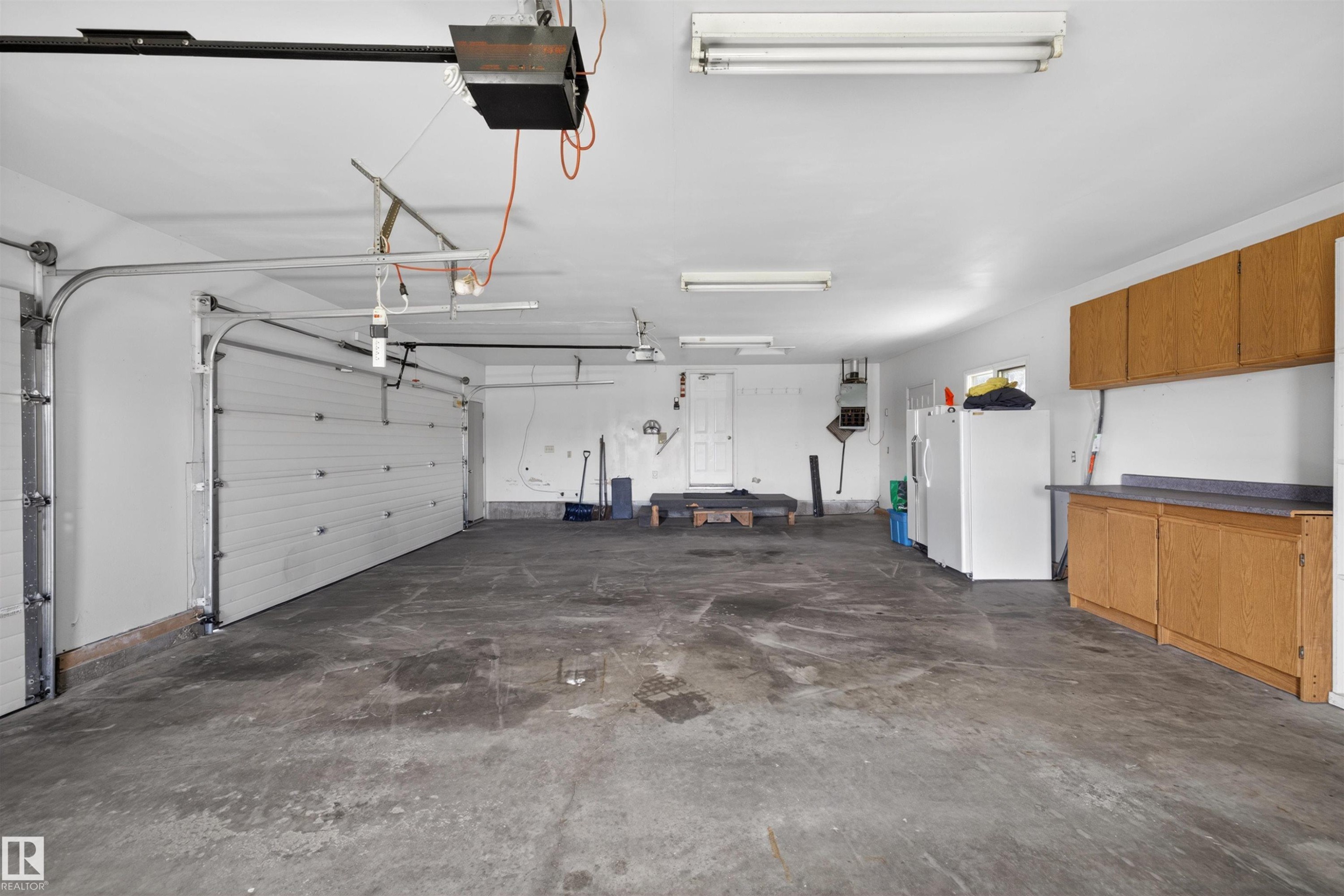 Spacious garage featuring two overhead doors, concrete flooring, and built-in wood-finish cabinetry with a countertop - 19403 Fort Road, Edmonton, AB - Indoor Photo Showing Garage